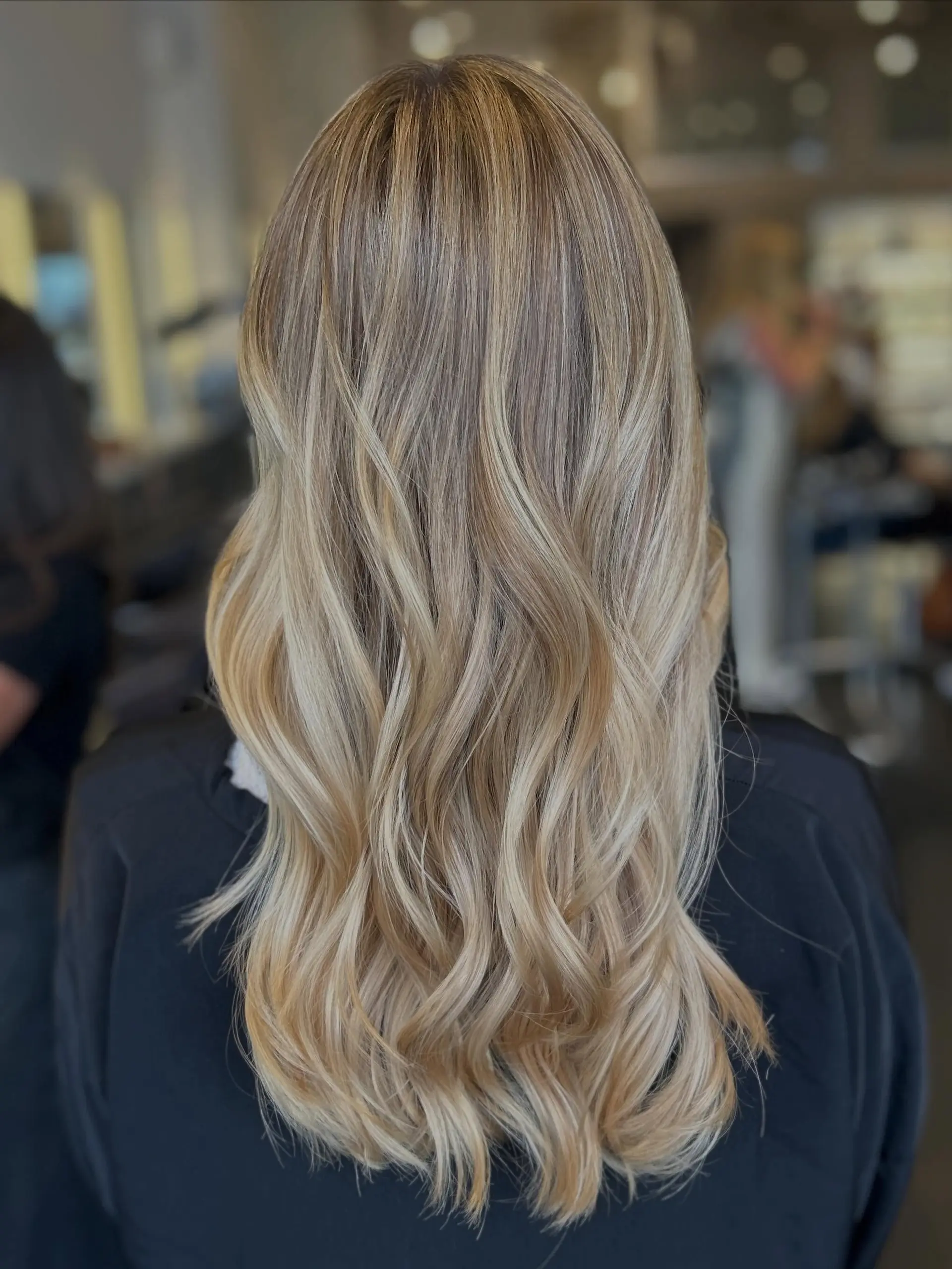 Long multi-tonal blonde hair with seamless full highlights styled in loose, flowing waves. 1