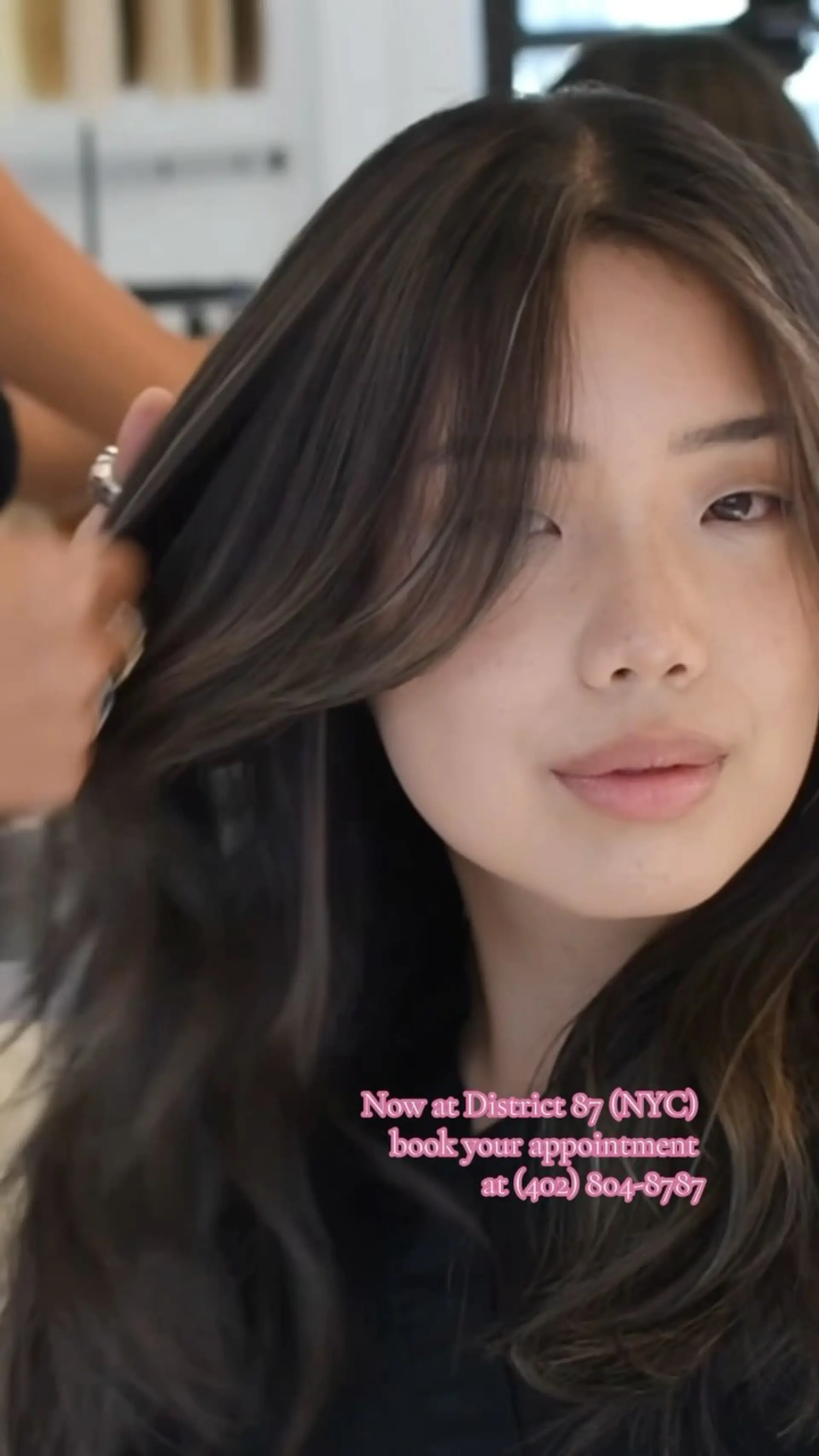 Dark brunette layered hair styled with soft volume and face-framing curtain bangs. The source post gives Sakura’s downtown NYC / District 87 booking information. Any displayed estimate uses Cooper West Hollywood’s starting-price menu; the pictured appointment’s venue and price are unverified. 1