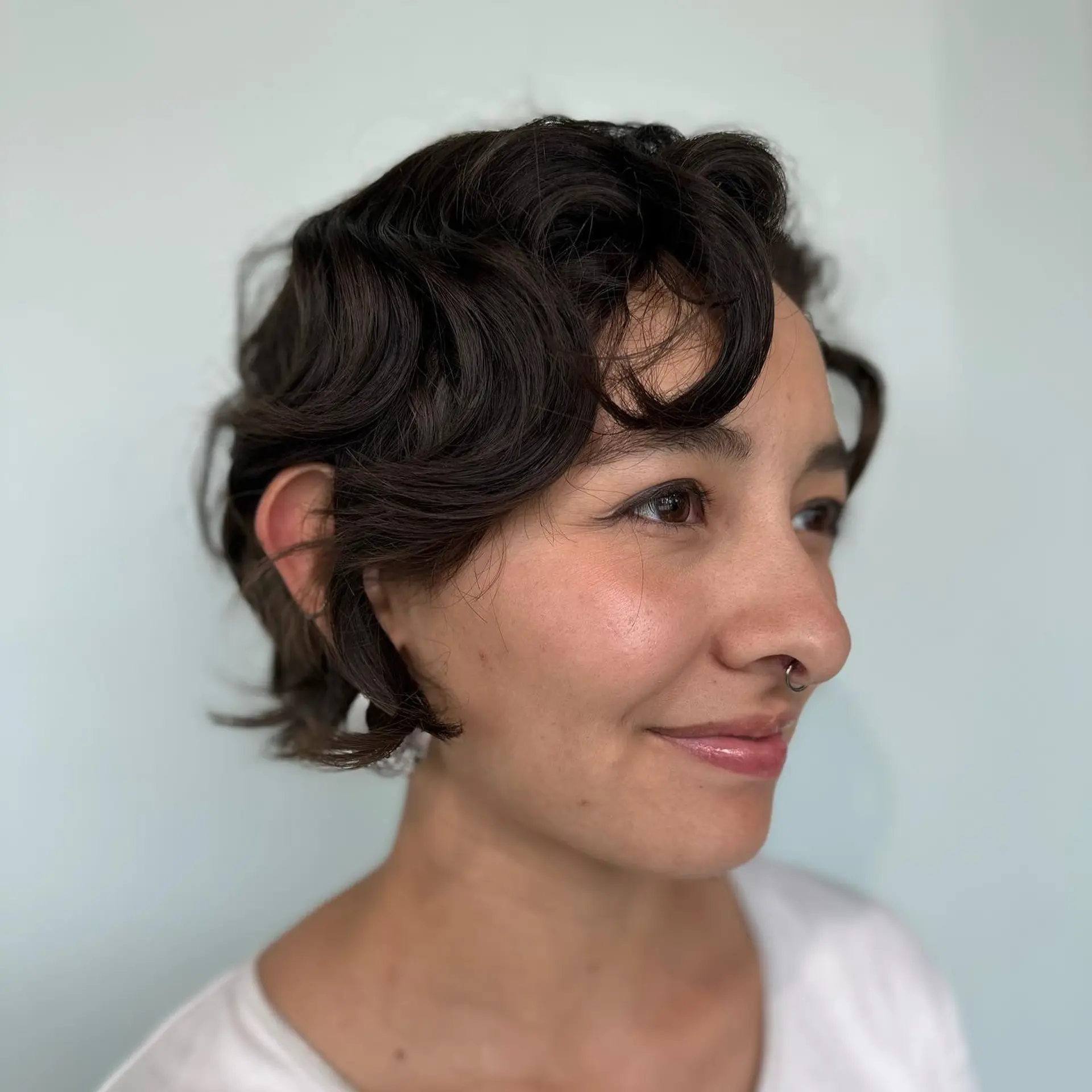 A textured bixie haircut in deep brown, styled with soft, piecey curls and face-framing waves. 1