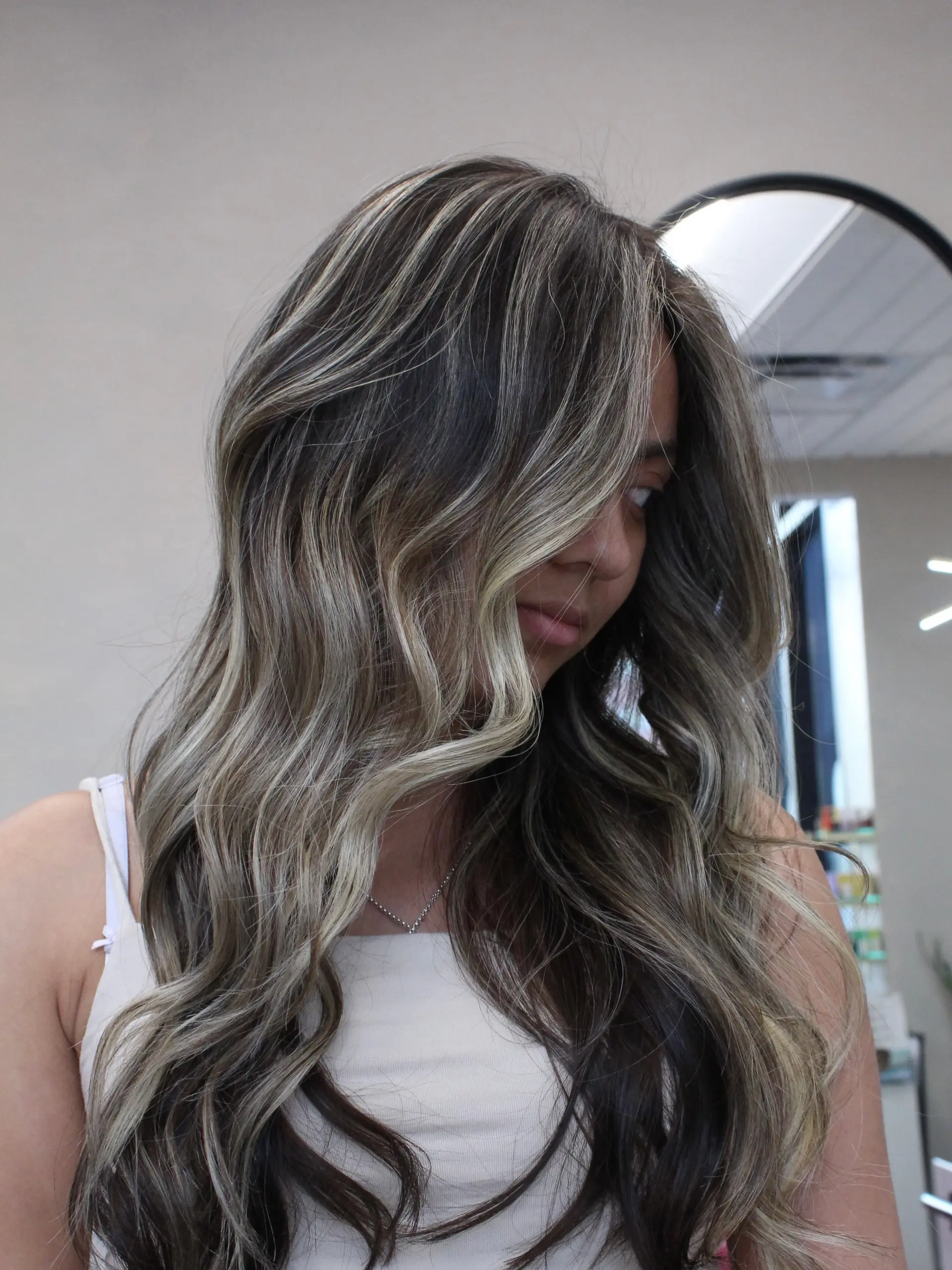 Long flowing brunette hair styled in loose waves with cool-toned ash blonde balayage highlights. 1