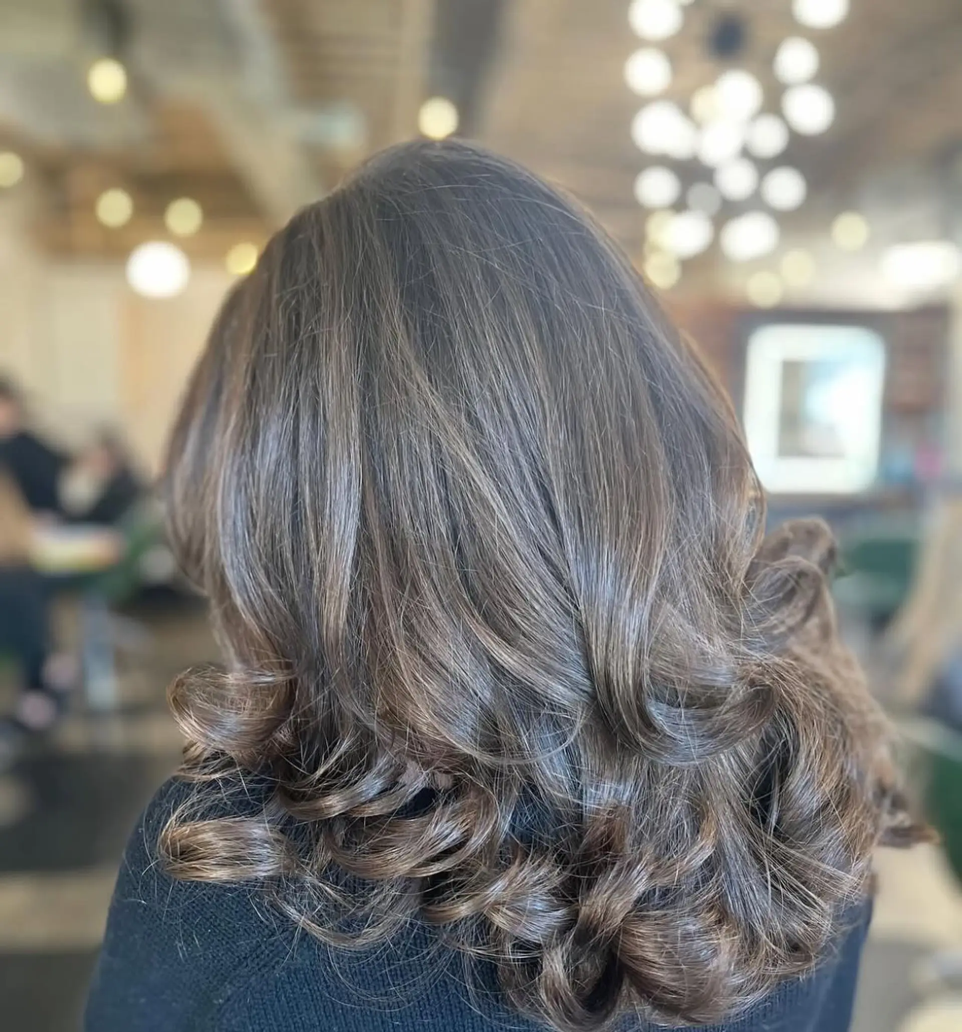 Medium-length layered brunette hair styled in a bouncy, voluminous blowout with flipped and curled ends. 1