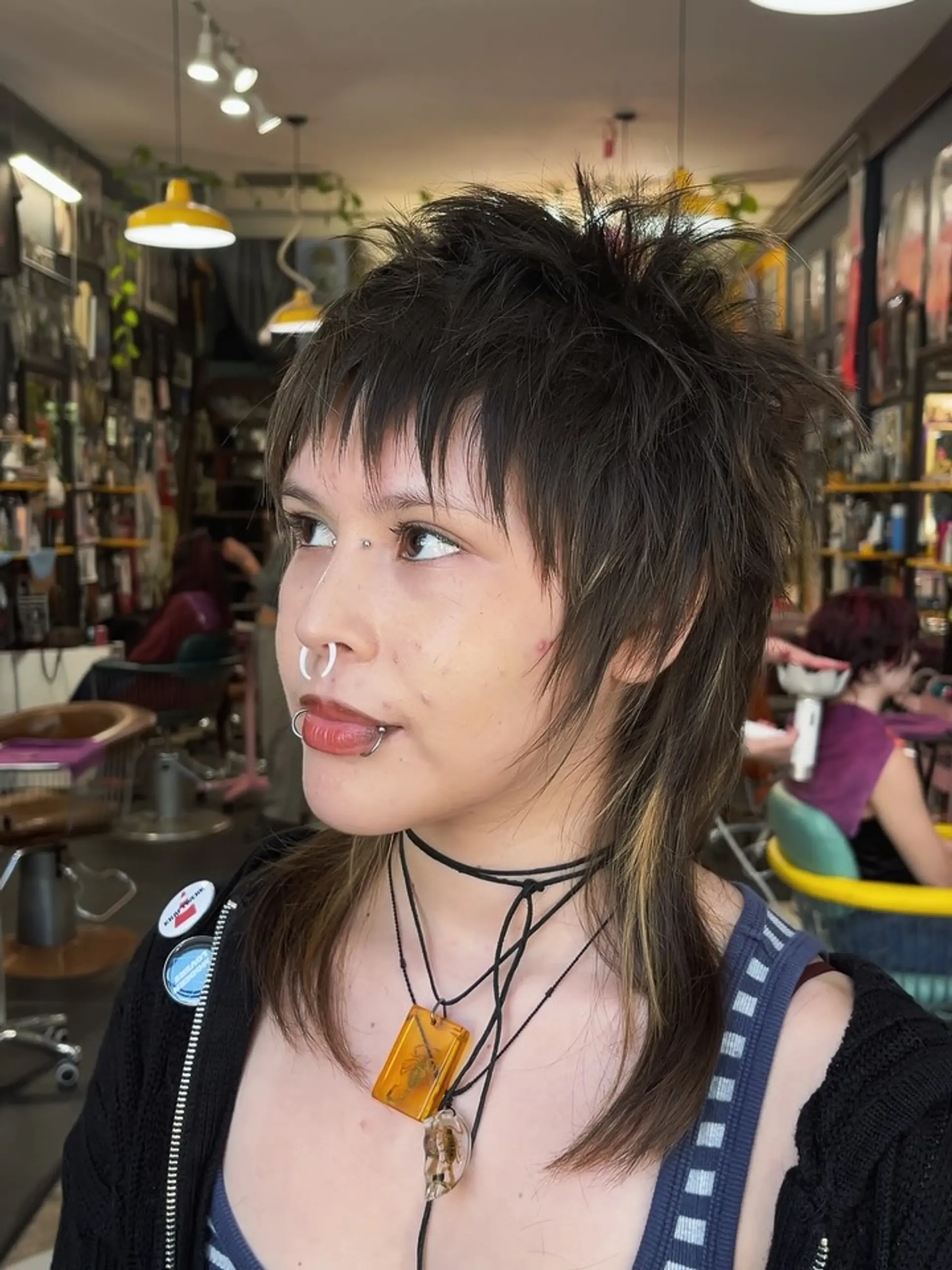 A choppy, textured mullet with short spiky crown layers, wispy micro bangs, and shoulder-length tail layers with peekaboo blonde highlights. 1