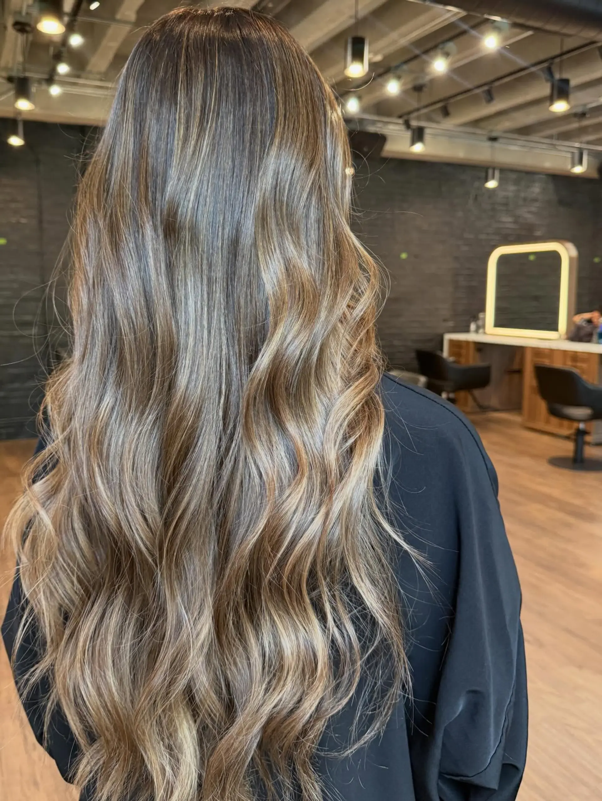 Long cascading brunette hair featuring seamlessly blended dimensional balayage highlights styled in soft waves. 1