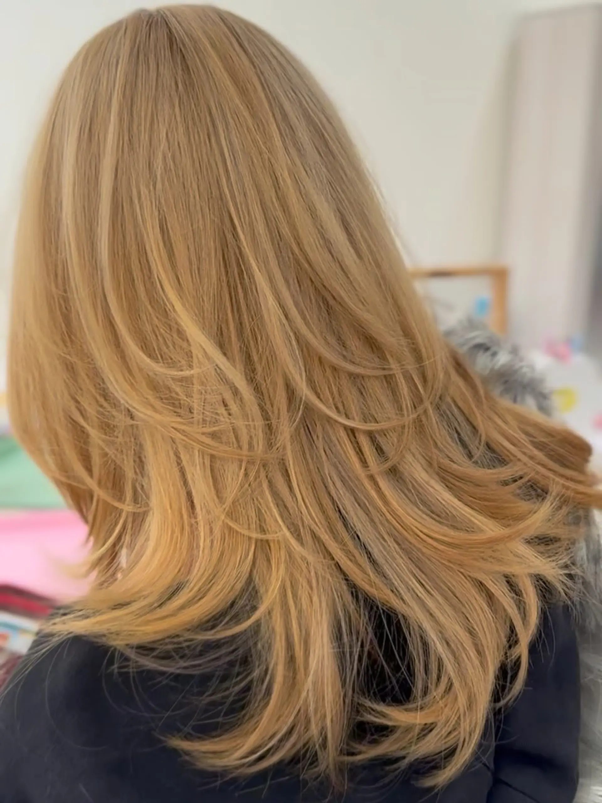Long warm golden blonde hair styled with feathered cascading layers and curved ends. 1