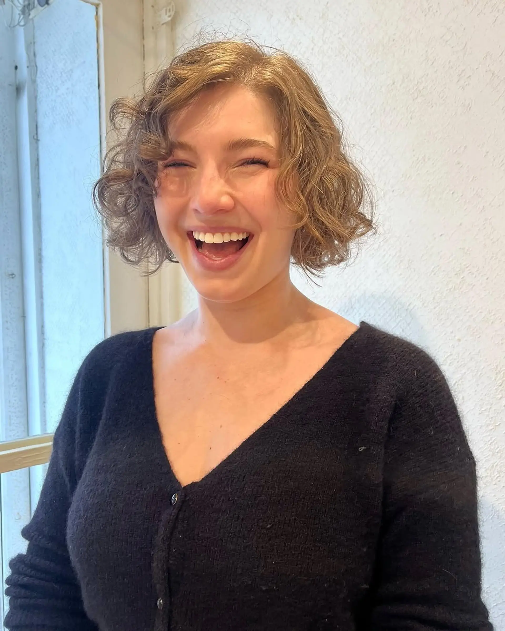 A short, wavy bob with light brown hair and golden highlights, featuring loose, soft waves for a natural, tousled appearance. 2