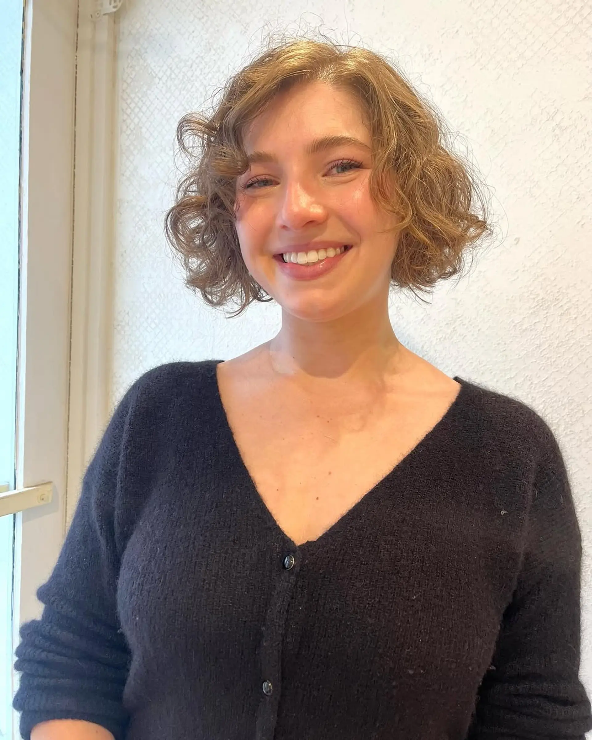 A short, wavy bob with light brown hair and golden highlights, featuring loose, soft waves for a natural, tousled appearance. 1