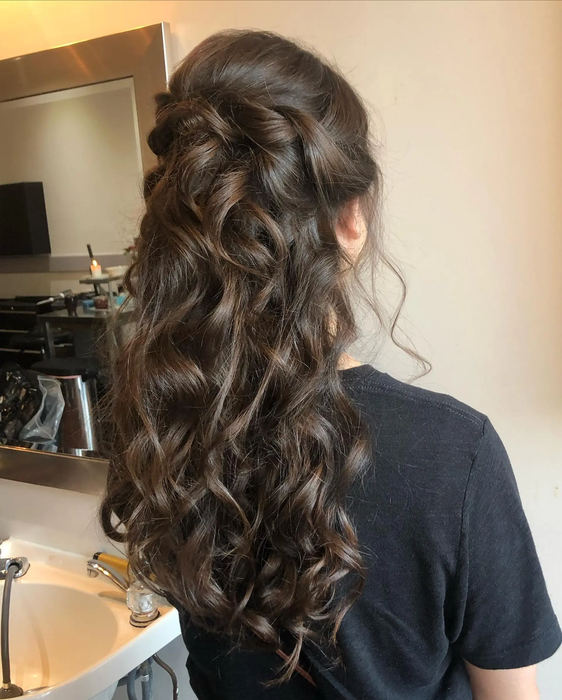 A romantic half-up bridal hairstyle featuring soft crown twists gathered neatly above tumbling, defined brunette curls. 1