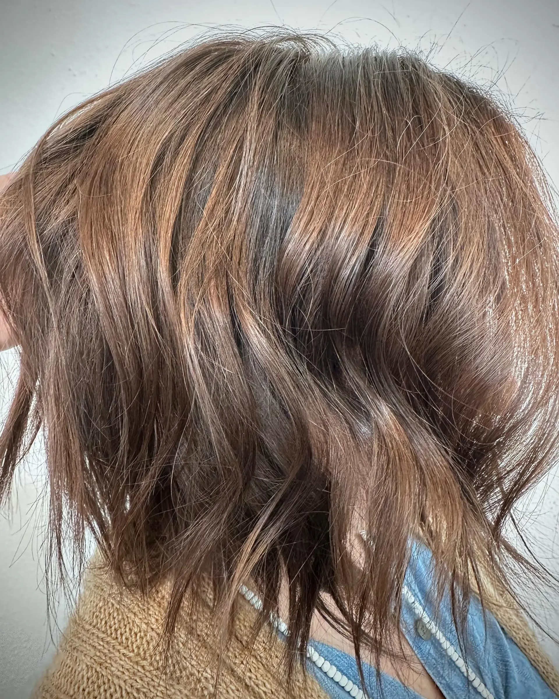 A textured chin-to-neck length brunette bob featuring subtle, sun-kissed warm caramel balayage highlights styled with soft, piecey bends. 1