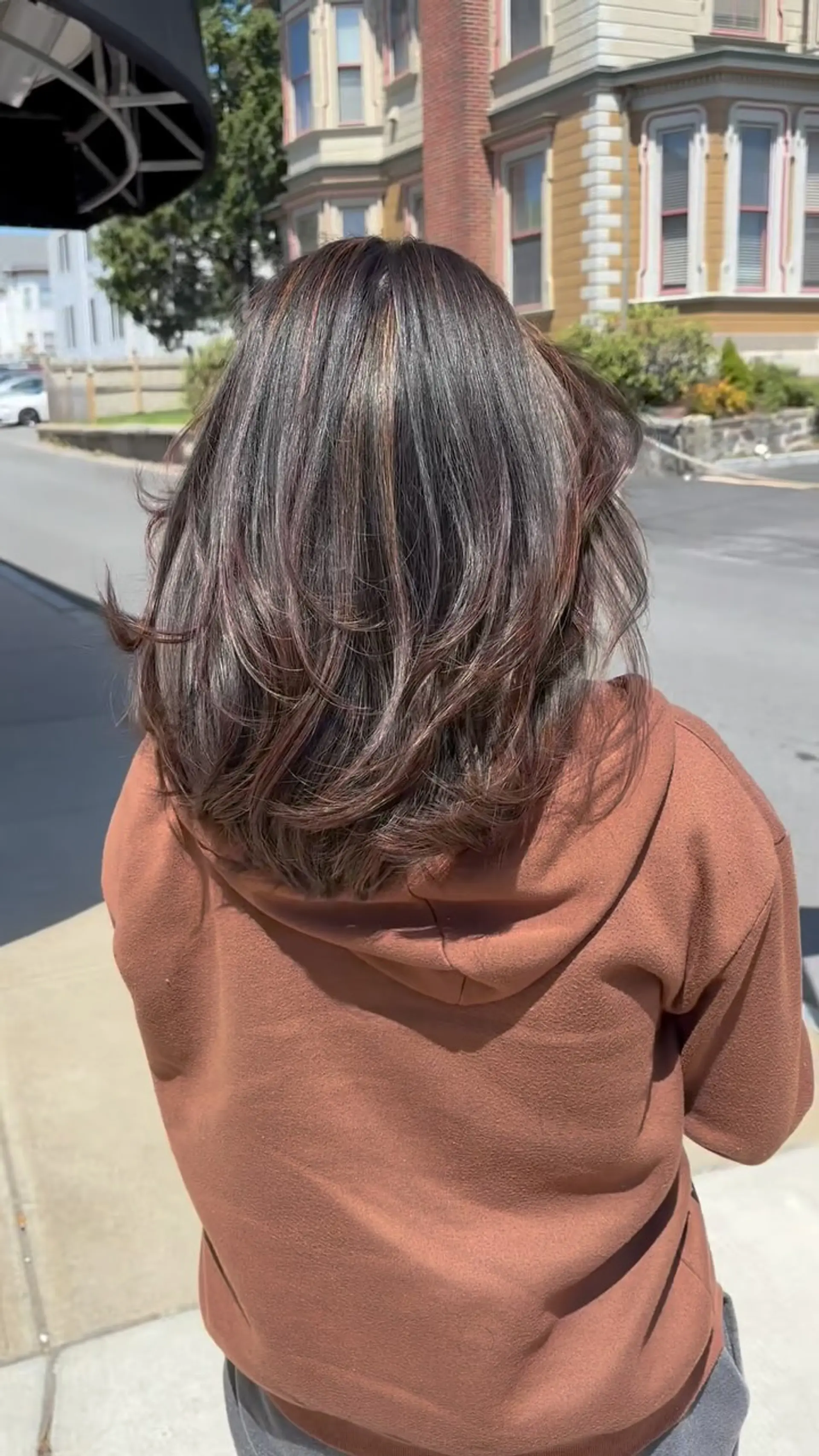 Medium-length dark brunette hair featuring face-framing layers, delicate warm copper highlights, and a soft, rounded blowout with curved ends. 1