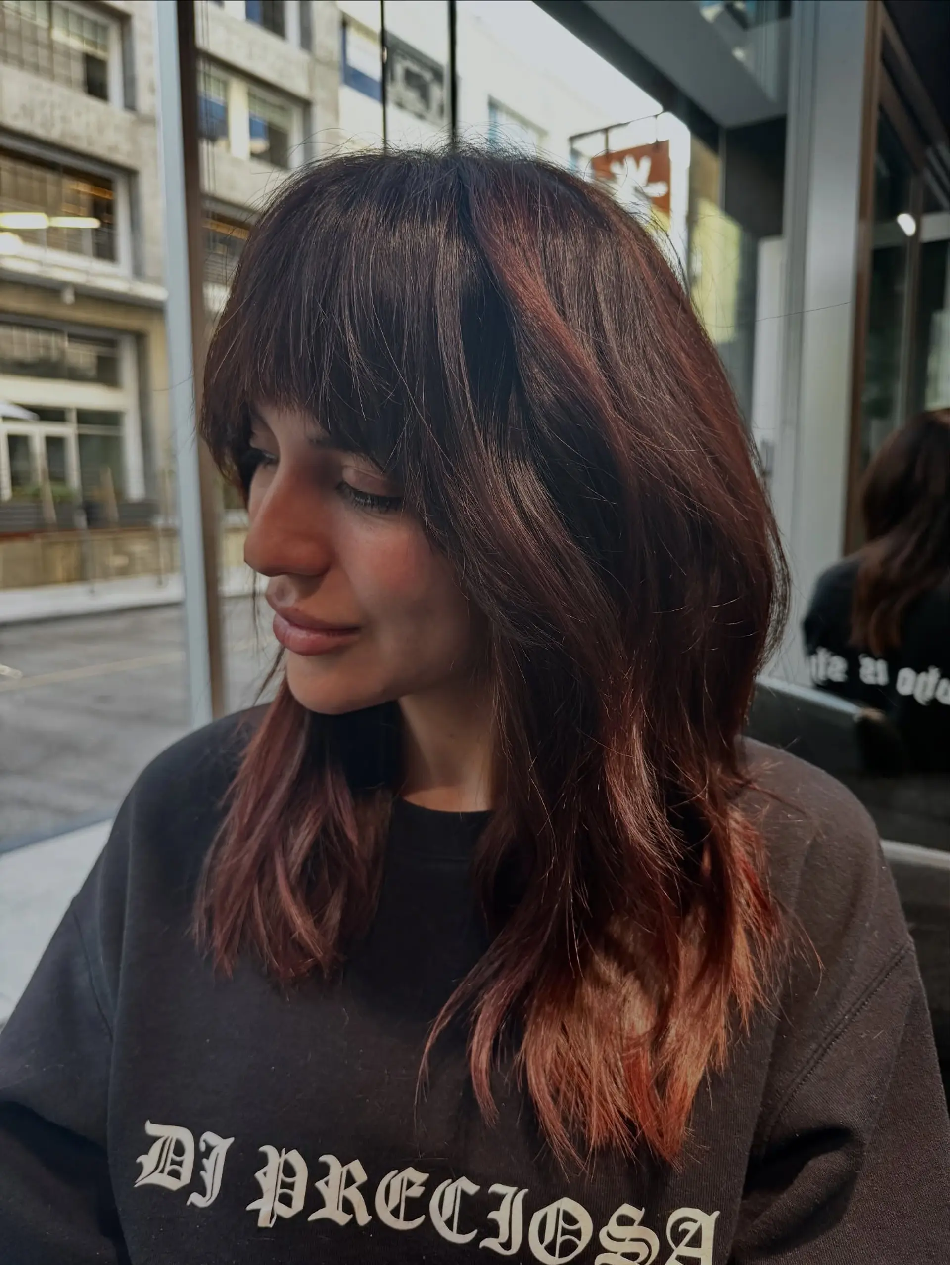 Medium-length layered haircut with a soft, full fringe and face-framing layers in warm reddish-brown tones. 1