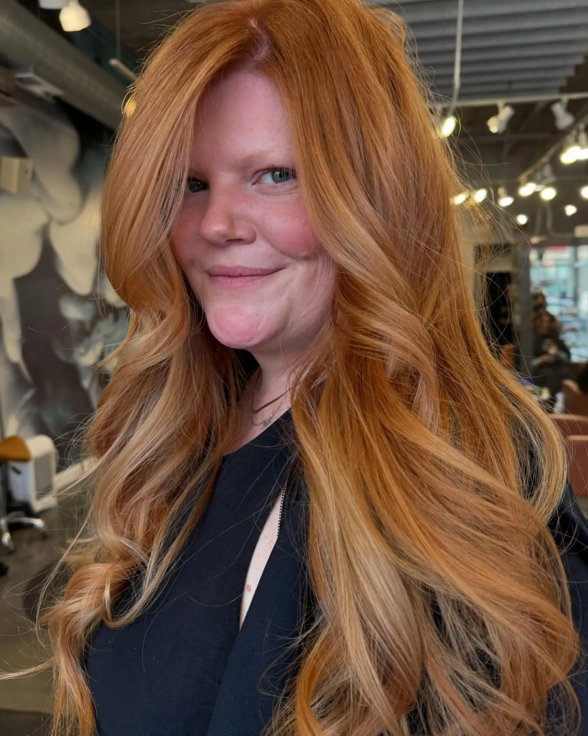 A long, wavy hairstyle with layered ends and face-framing layers, highlighted by a warm copper color with blonde balayage. 1