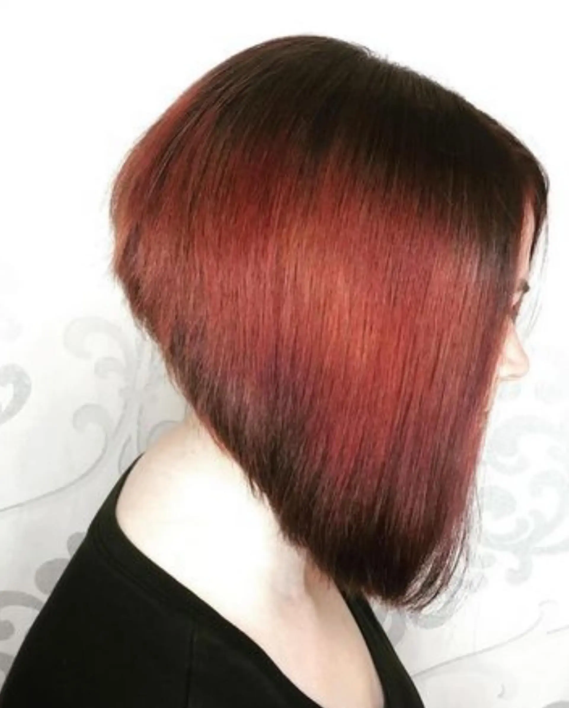 A sleek, dramatically angled inverted bob cut styled straight with rich auburn and red tones. 1