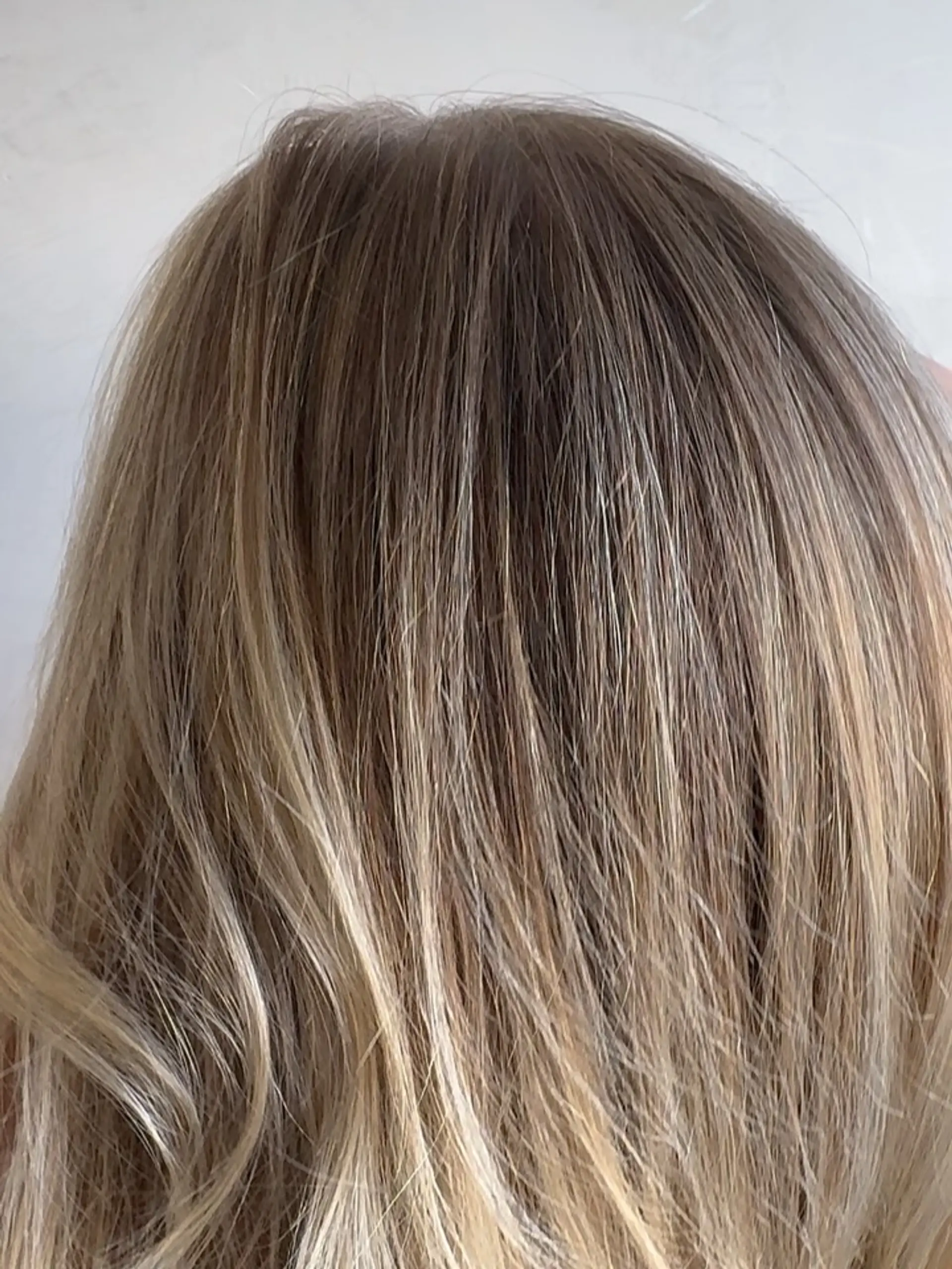 A close-up view of dimensional lived-in blonde hair featuring seamless babylights blended with a natural base. 1