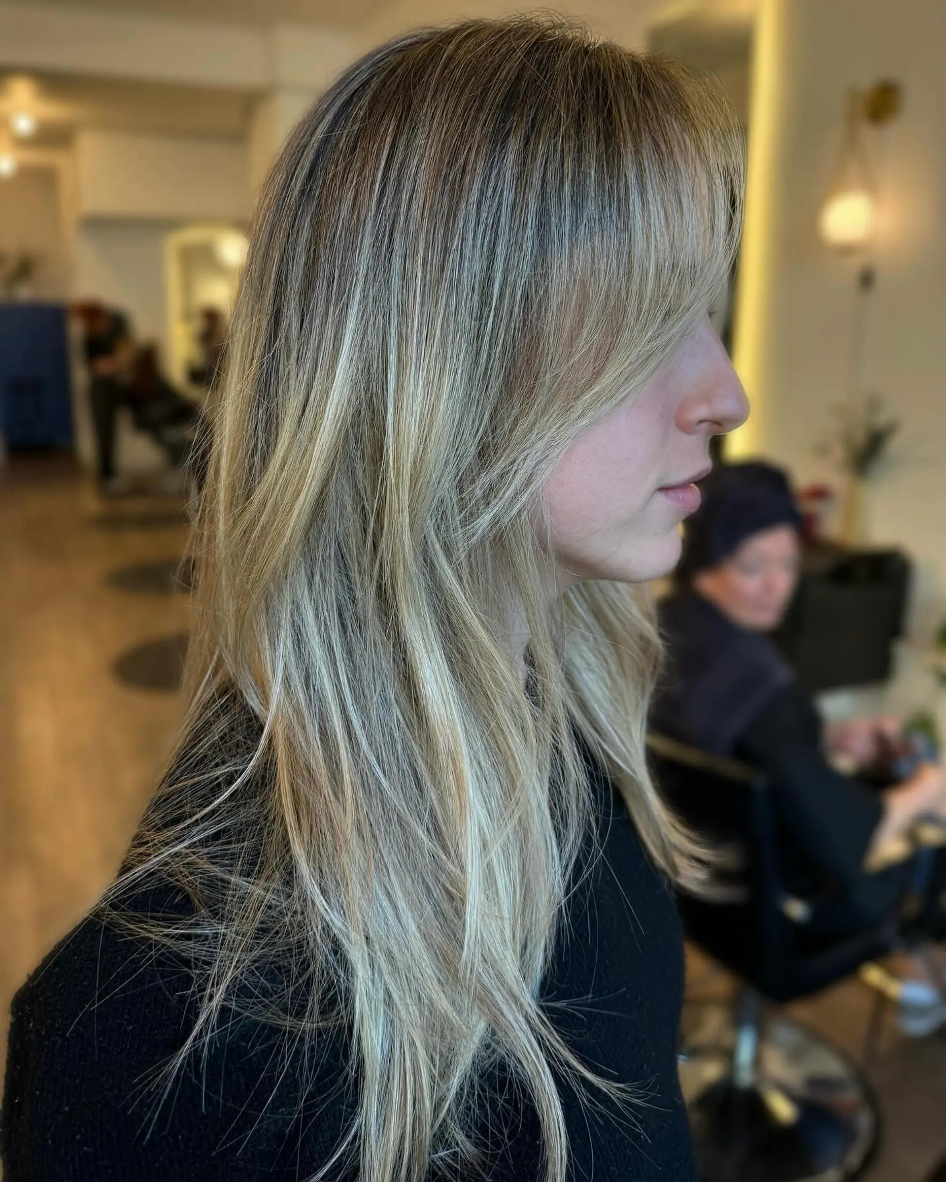 Long layered dimensional blonde hair styled straight with textured face-framing bangs. 1