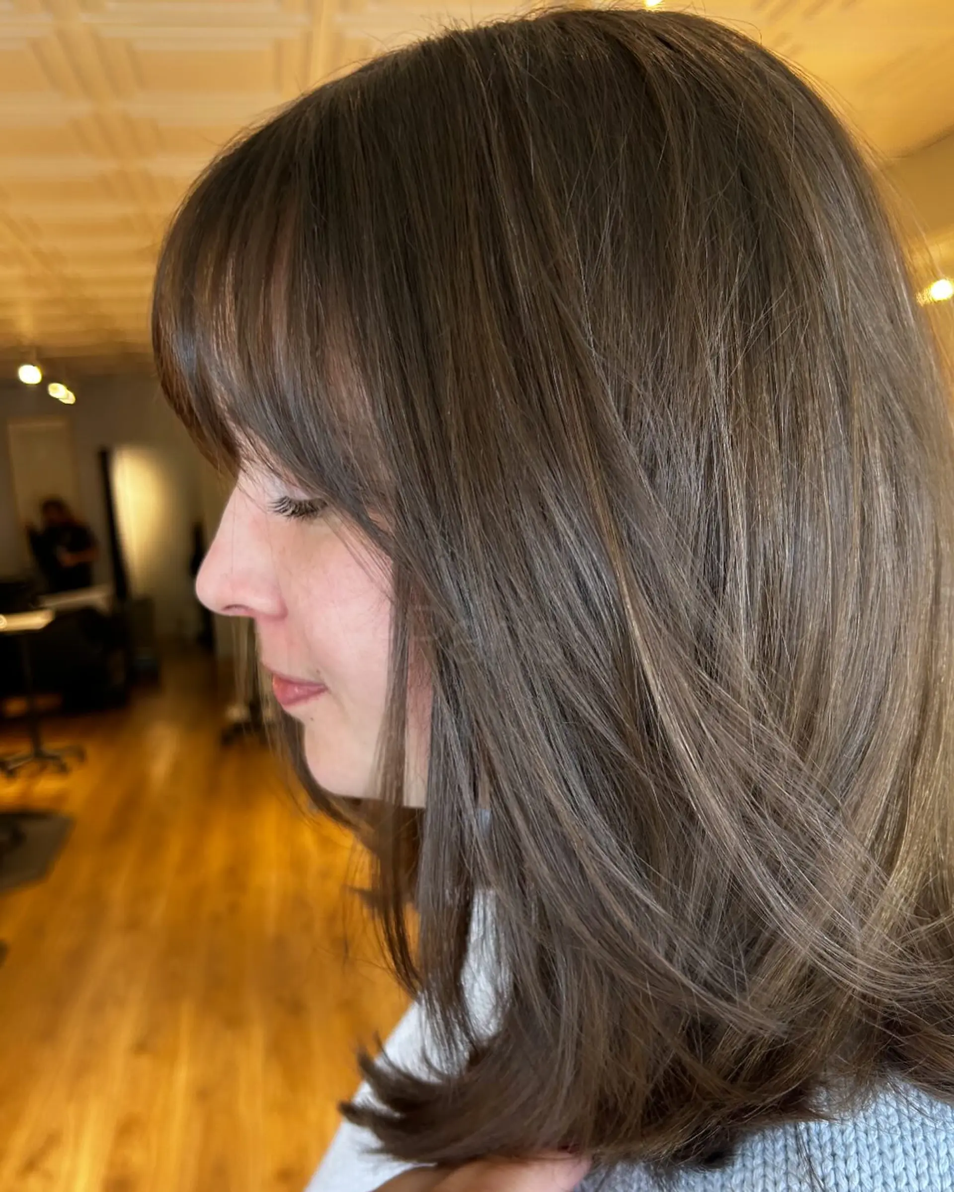 Medium-length layered brunette haircut with soft face-framing layers and wispy textured bangs. 1