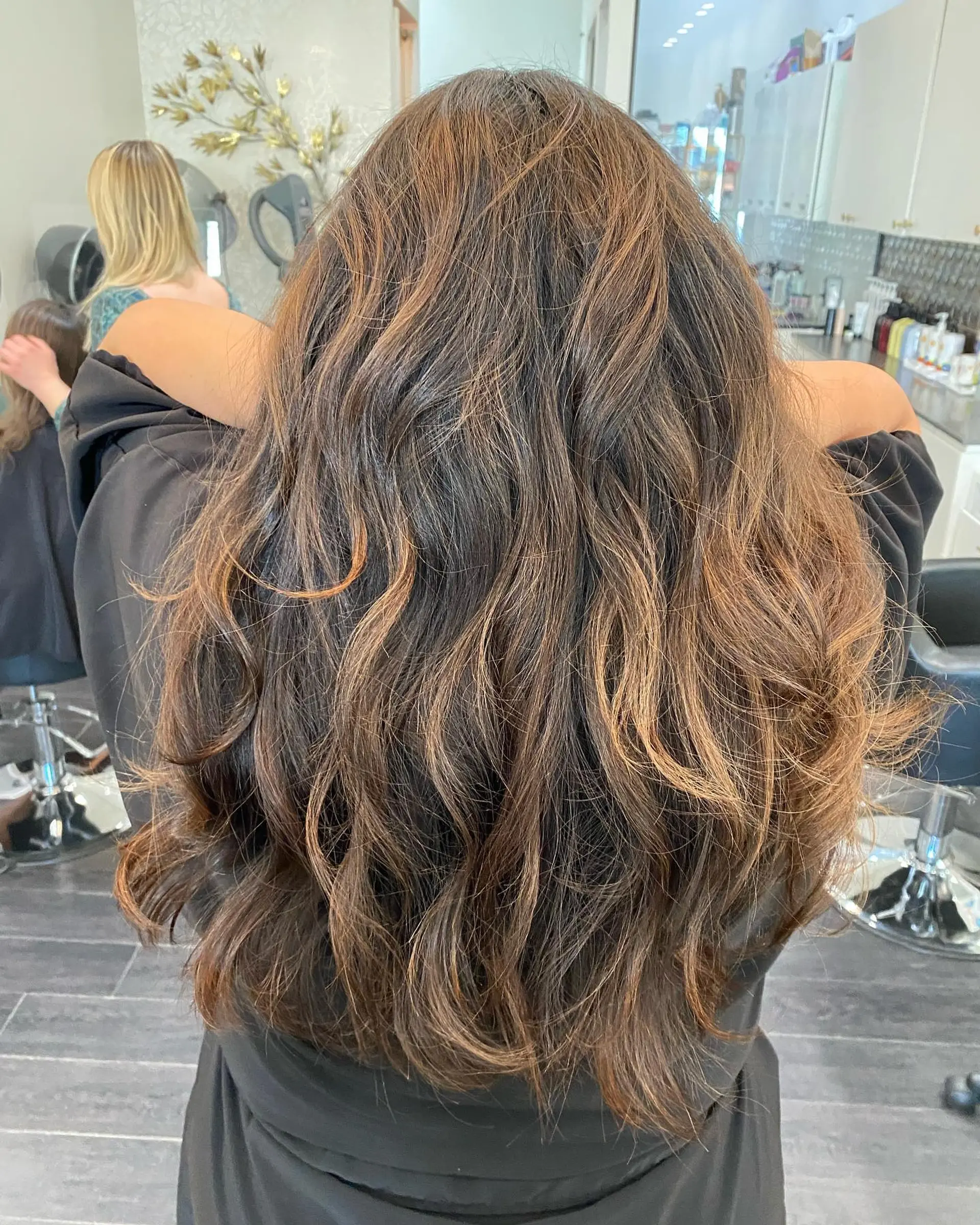 Long, layered dark brown hair styled in soft, textured waves with warm caramel and bronze highlights. 1