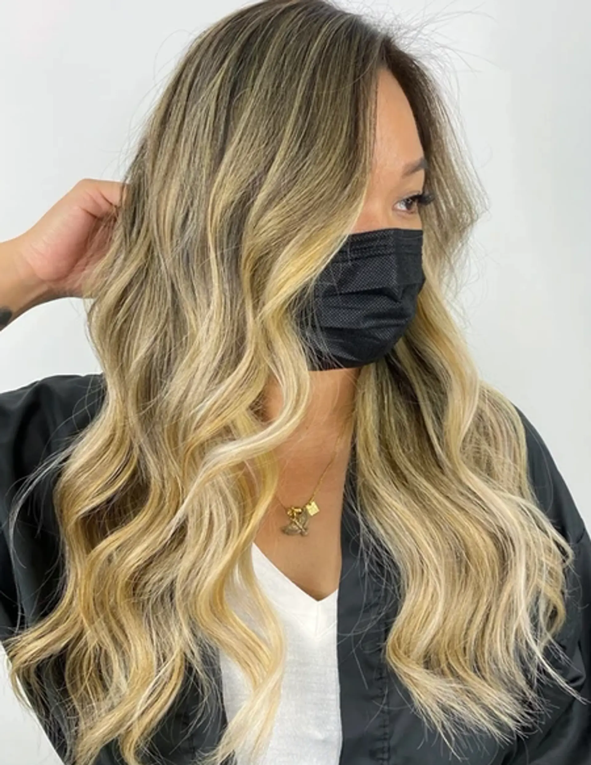 A long, wavy hairstyle with a balayage effect blending dark brown roots with light blonde and golden hues. Featuring loose waves, a side part, and soft, face-framing layers for added elegance and dimension. 1