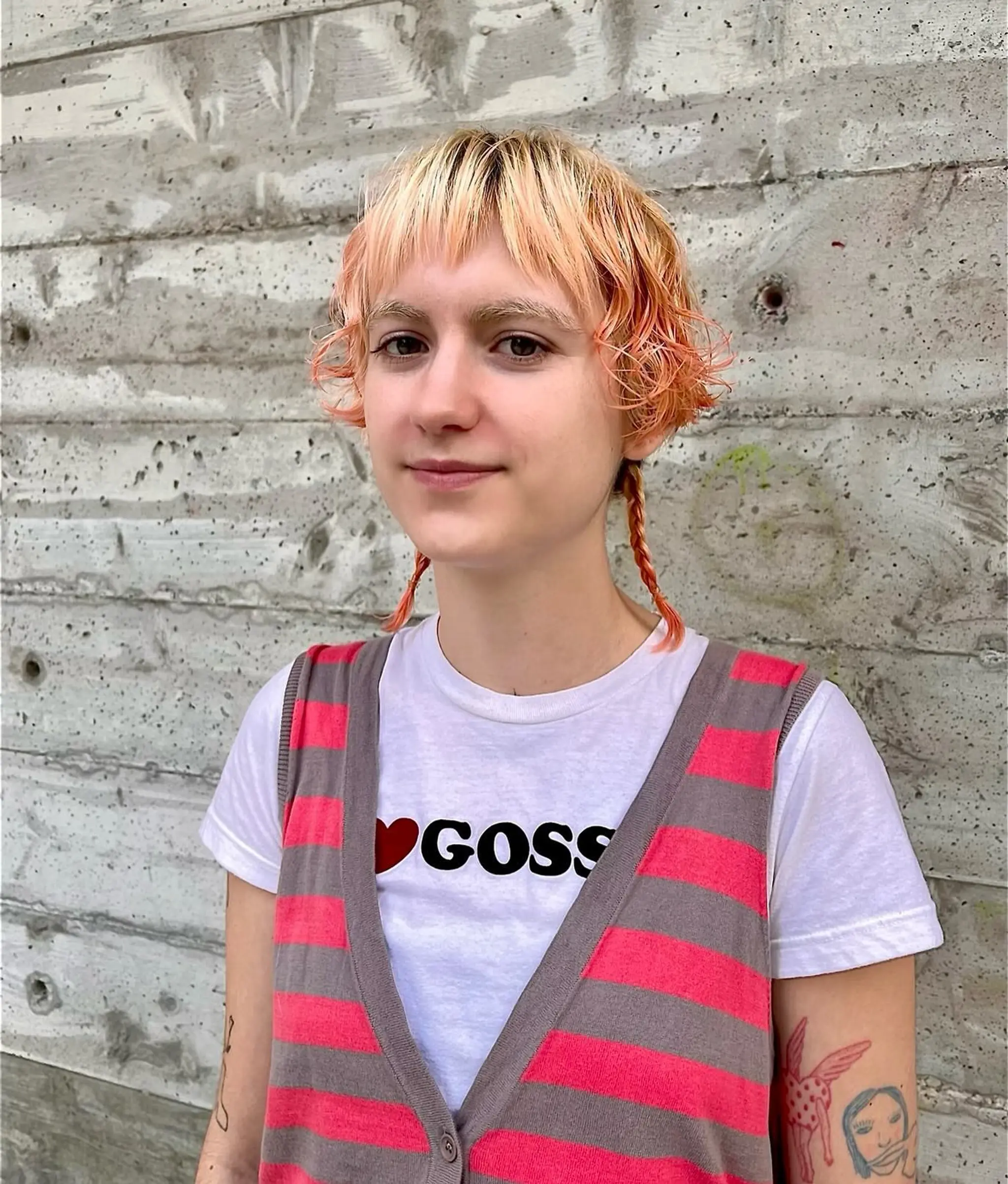 A wavy pixie cut with a peach and blonde color blend, featuring textured layers, a choppy fringe, and braided accents.