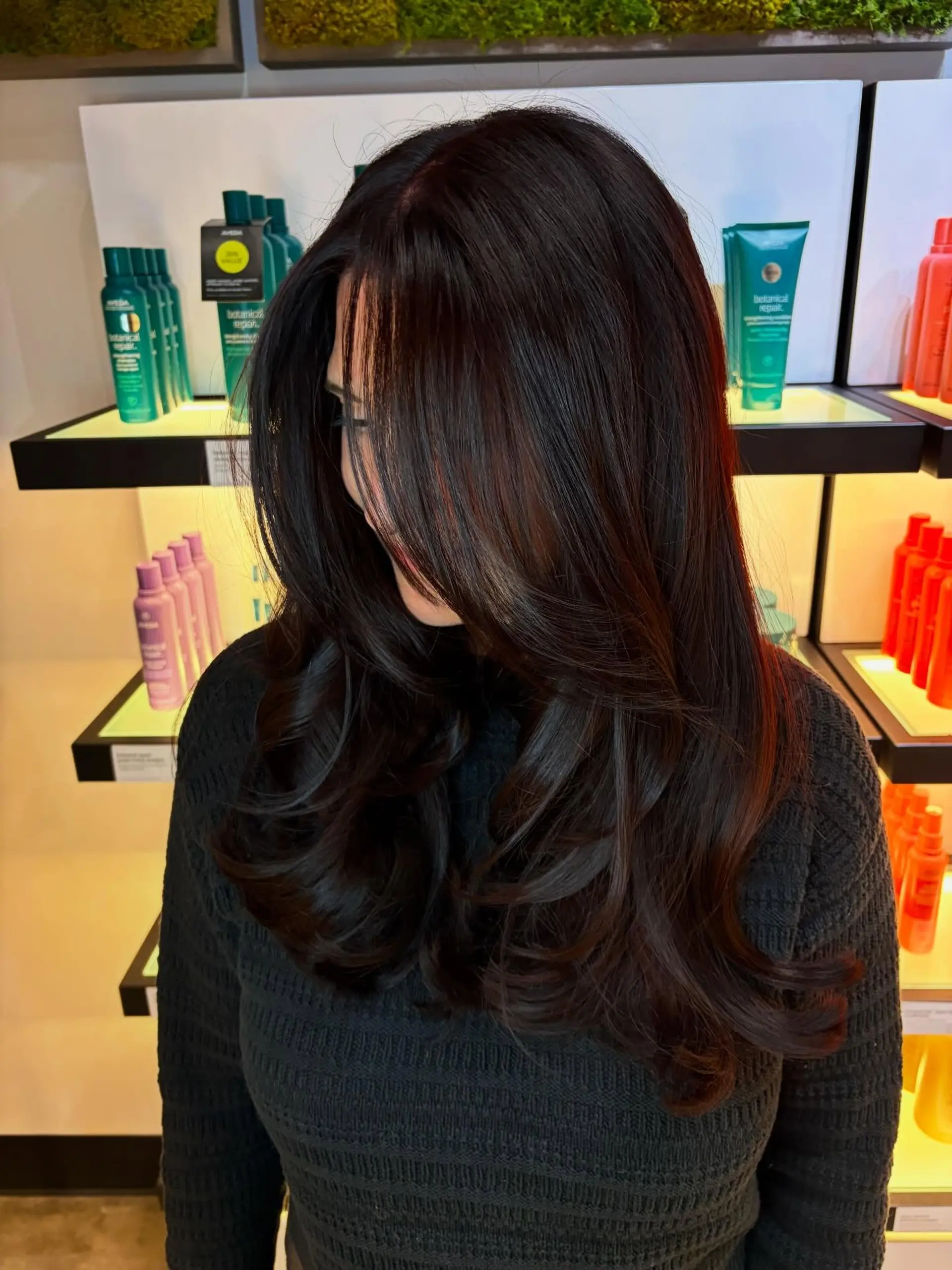 Glossy dark brunette long hair cut with cascading layers and styled into a voluminous, bouncy blowout with curled ends. 1