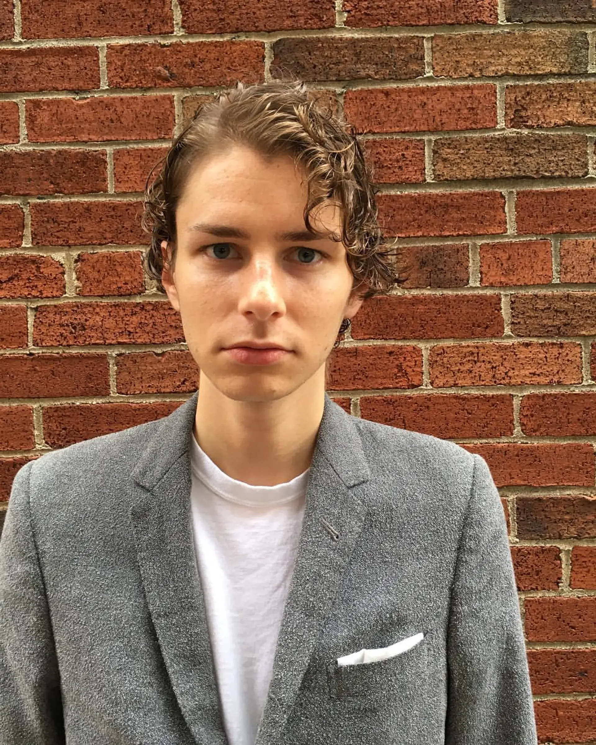 Short, light brown wavy hair with a slightly wet look, softly defined waves, and a neat, layered structure, giving a relaxed yet stylish appearance. 1