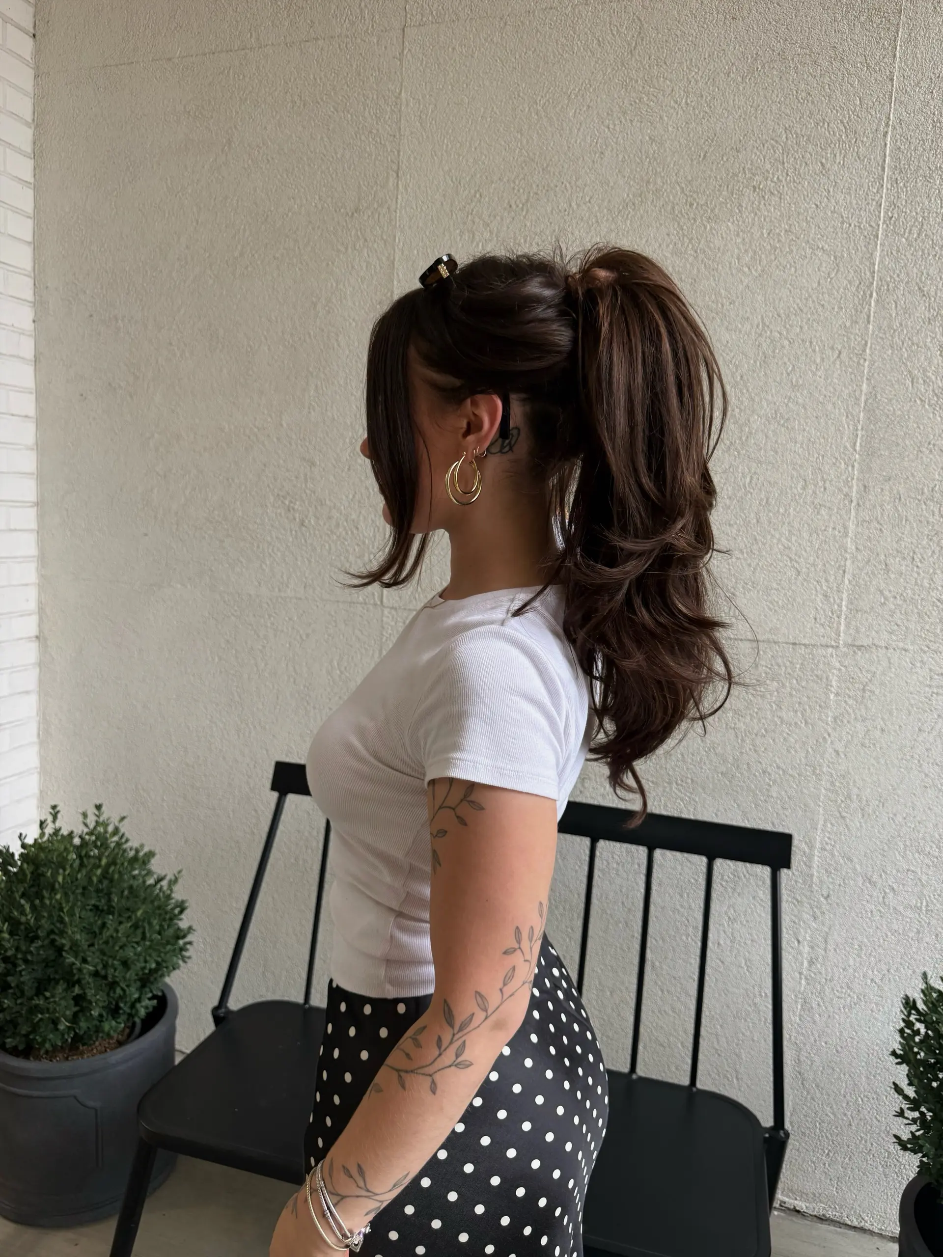 A glamorous, full-bodied high ponytail styled with soft romantic waves and face-framing tendrils in a rich dark brunette tone. 1