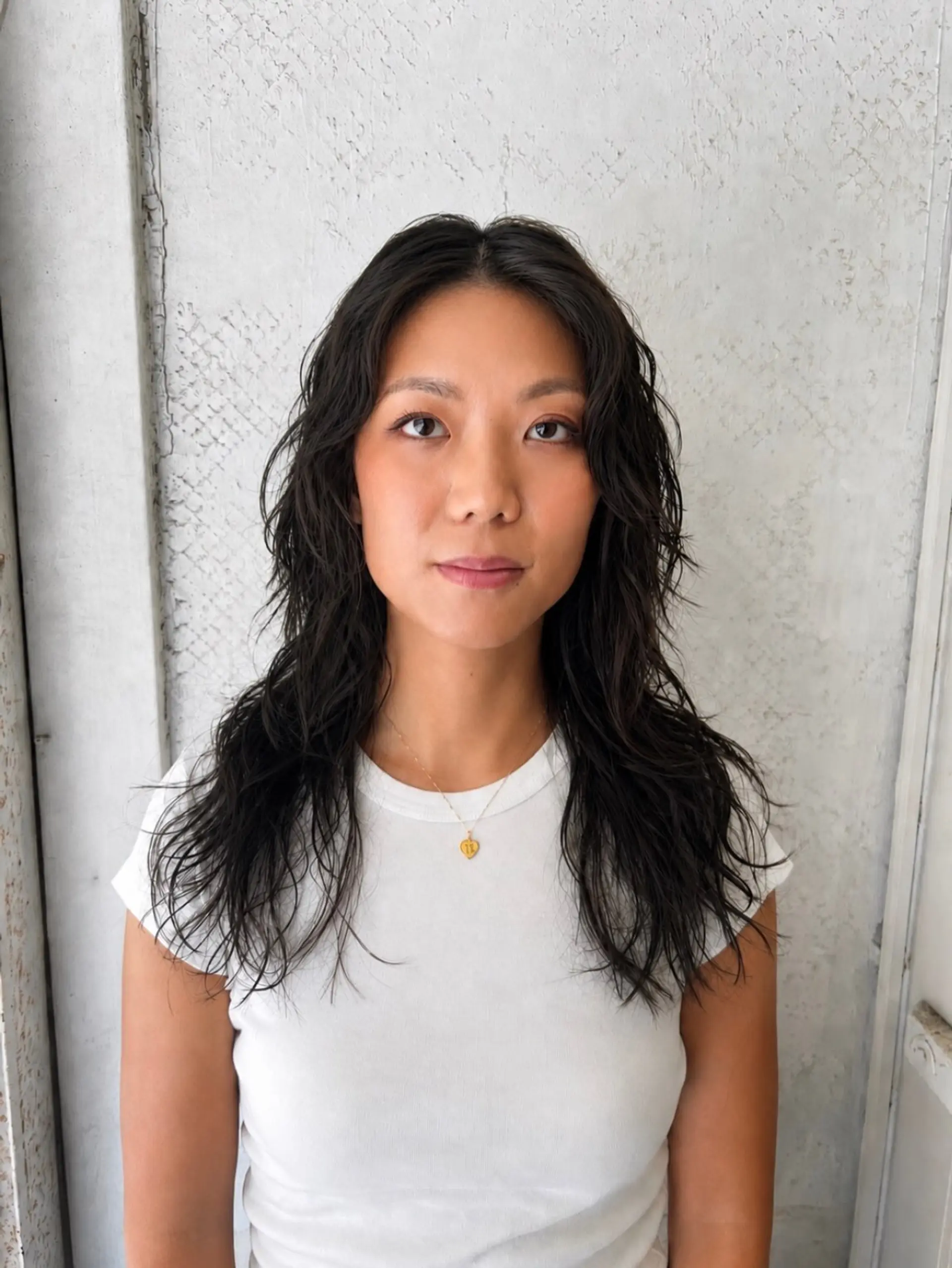 Medium-length dark hair styled with textured, tousled perm waves and layered ends. 1