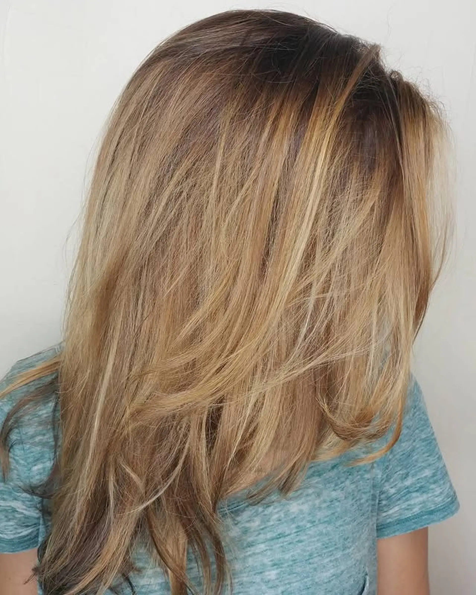 A layered long hairstyle with blended color from brown roots to blonde highlights. 1