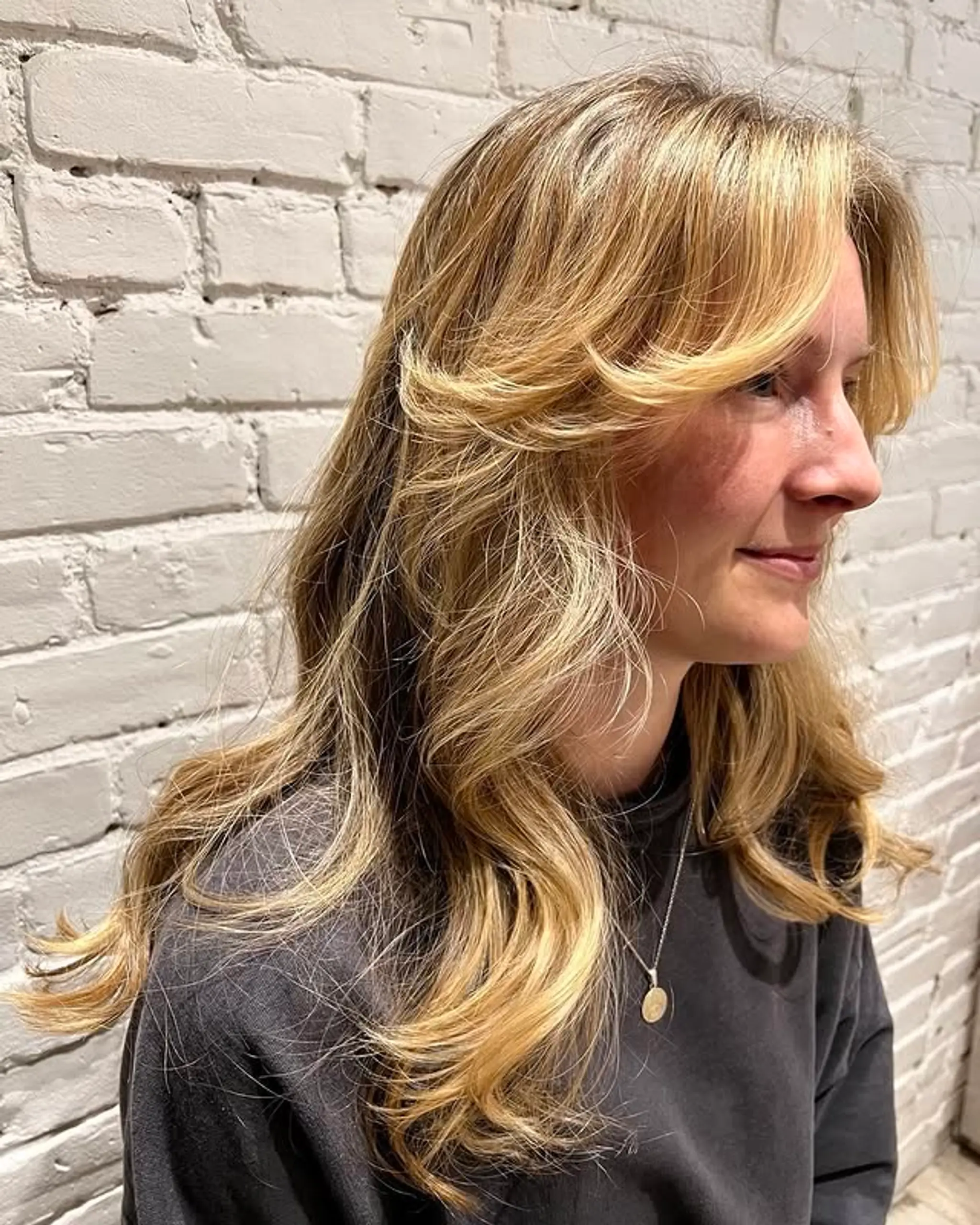 This hairstyle features long, wavy layers that frame the face beautifully, complemented by trendy curtain bangs.