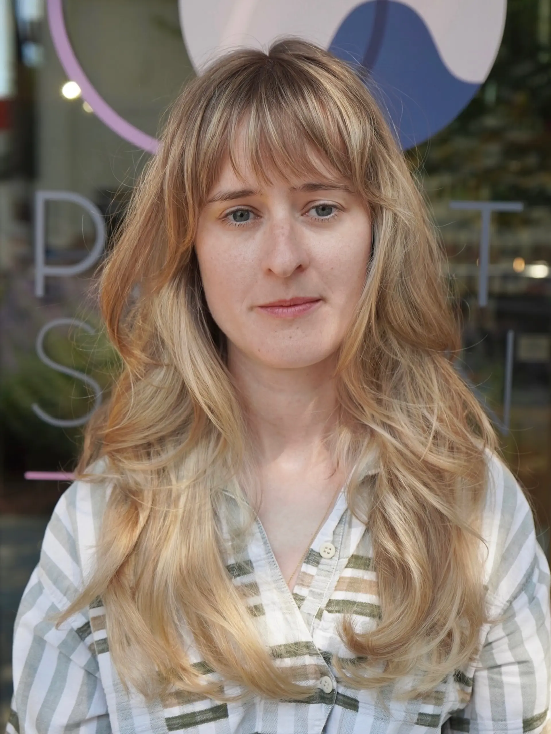 Long warm golden blonde layered haircut featuring soft wavy ends and a full wispy fringe bang. 1