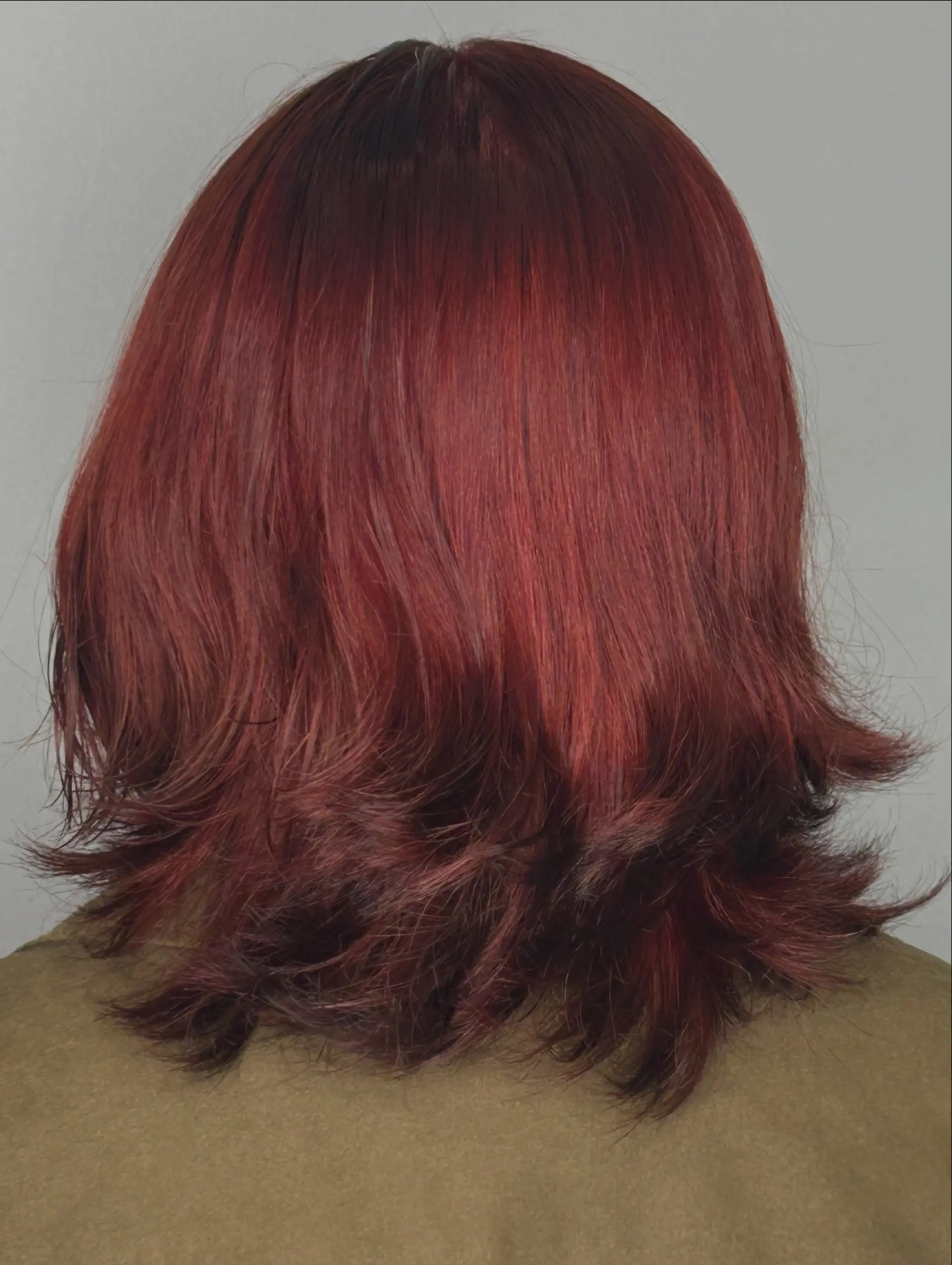 A medium-length layered haircut featuring rich auburn-red color with feathered, flipped ends. 1
