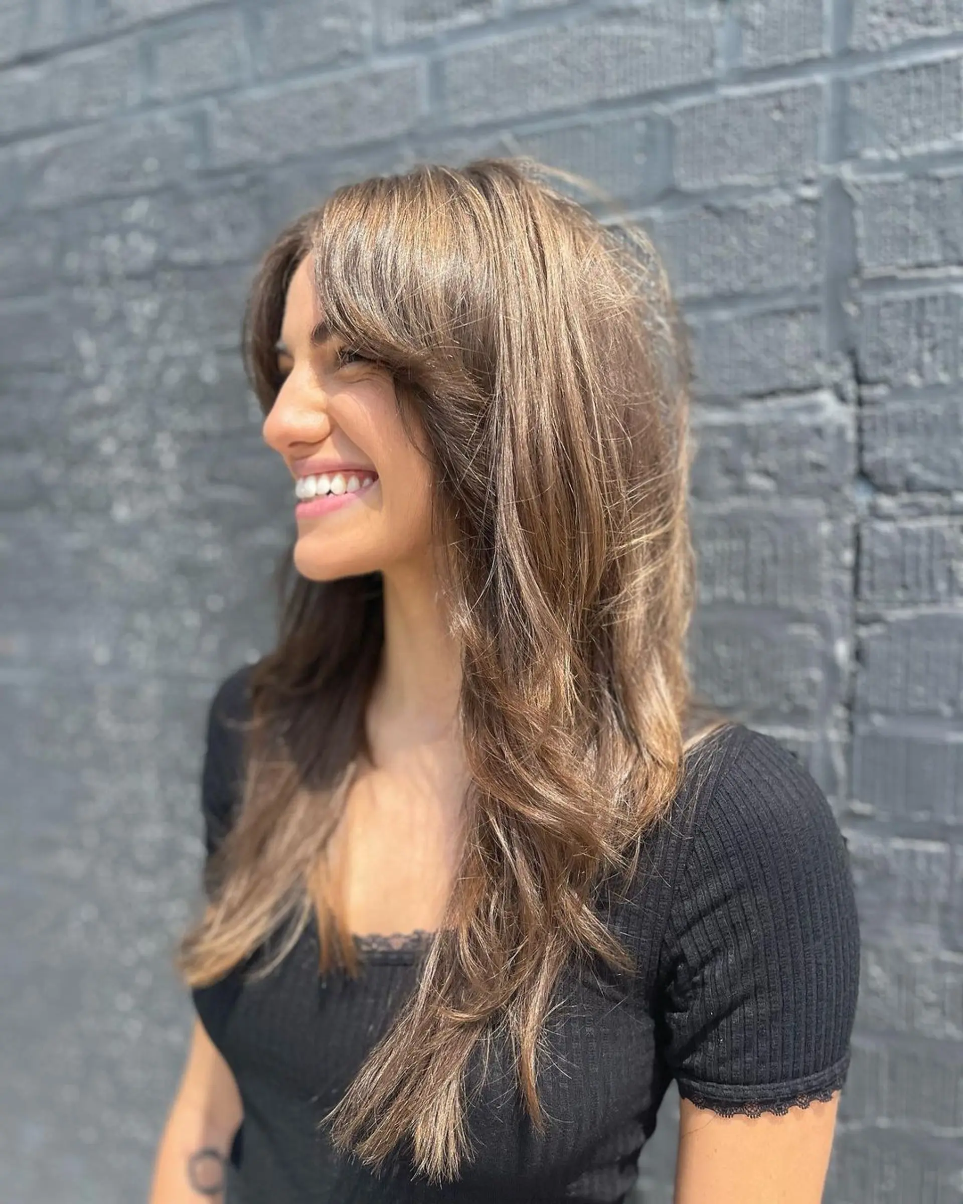 Long, warm brown wavy hair with layered cut and soft waves. Subtle face-framing fringe and natural highlights for a sun-kissed look. 1