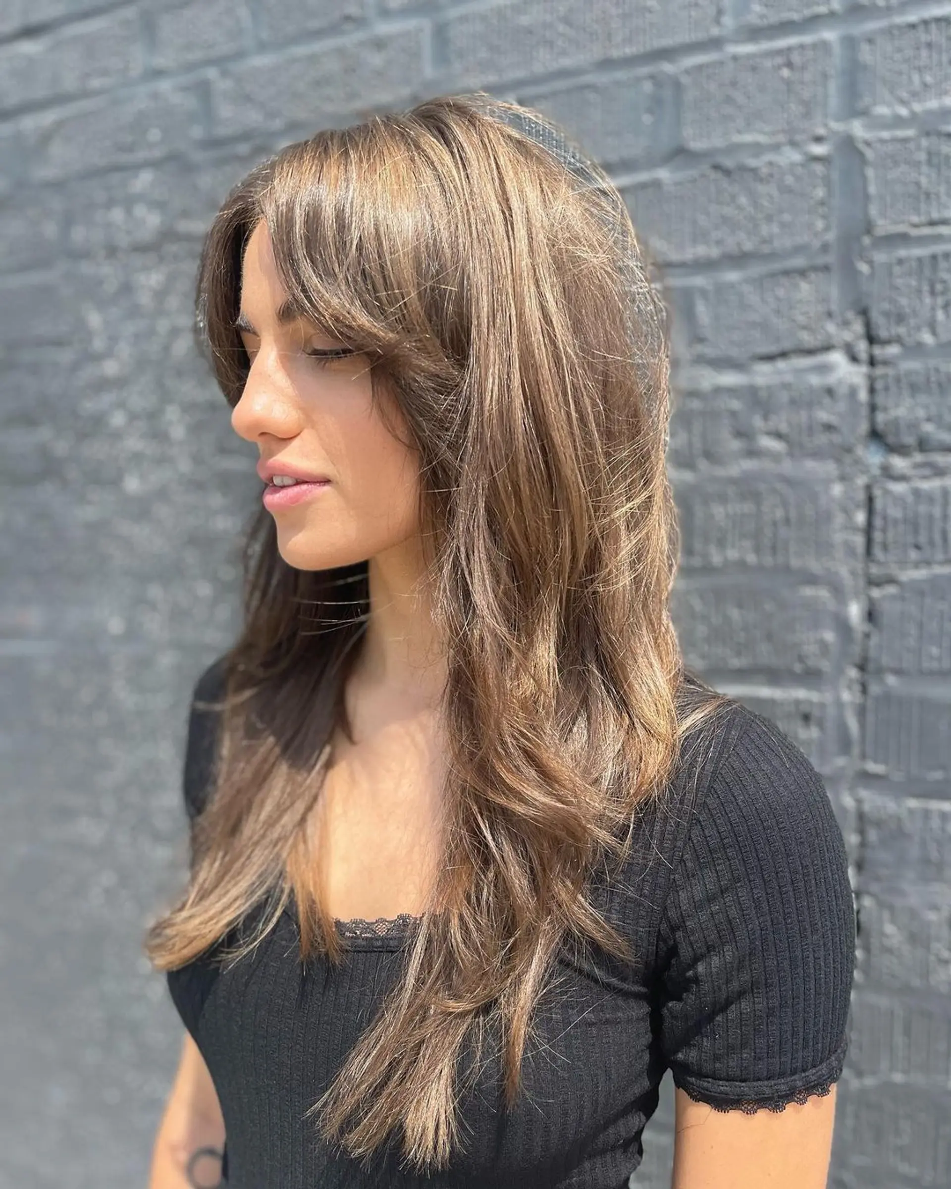Long, warm brown wavy hair with layered cut and soft waves. Subtle face-framing fringe and natural highlights for a sun-kissed look. 2