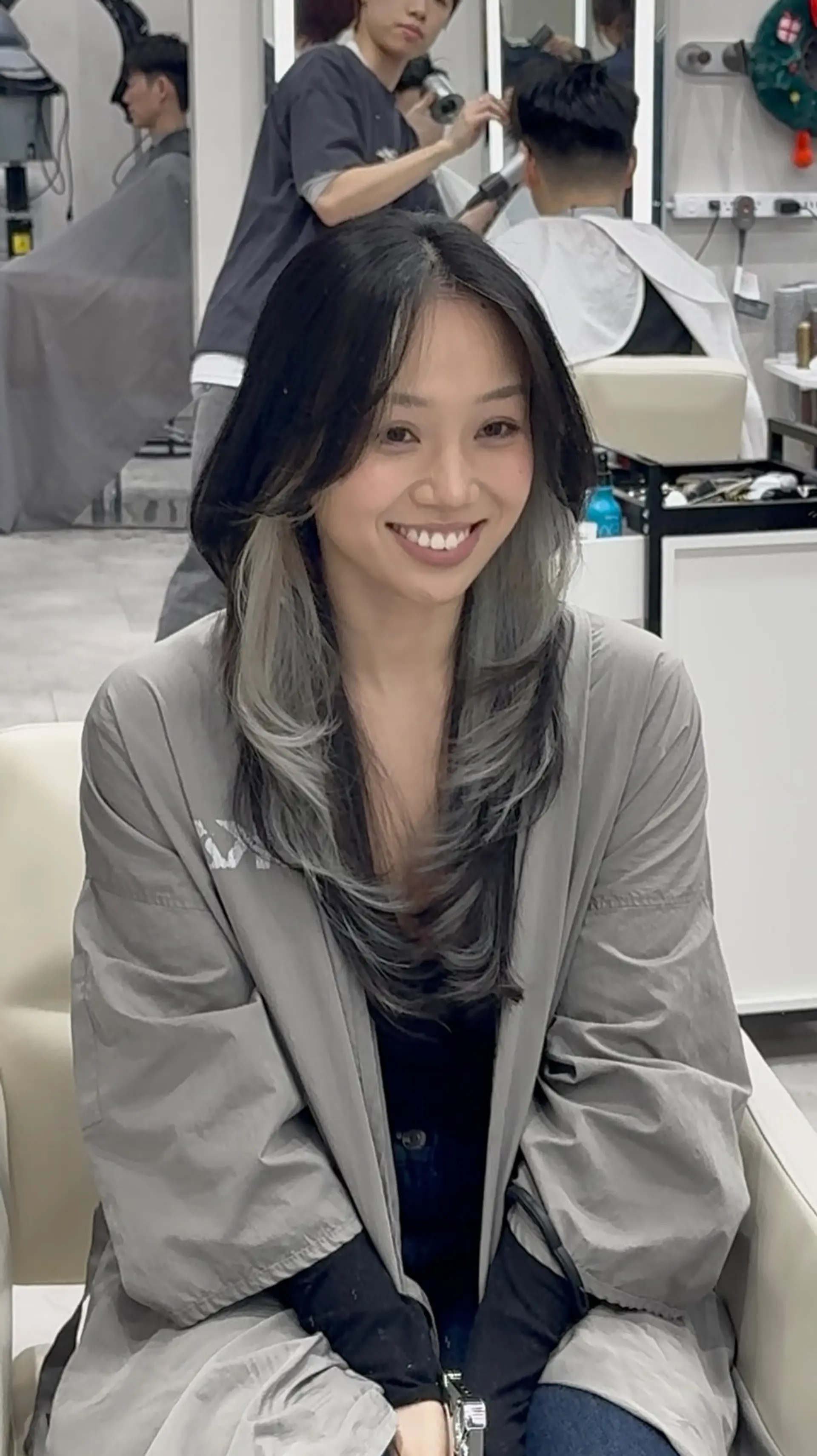 Chest-length layered haircut styled with soft inward curves, featuring a dark overlay with an ash grey under-color contrast. 1