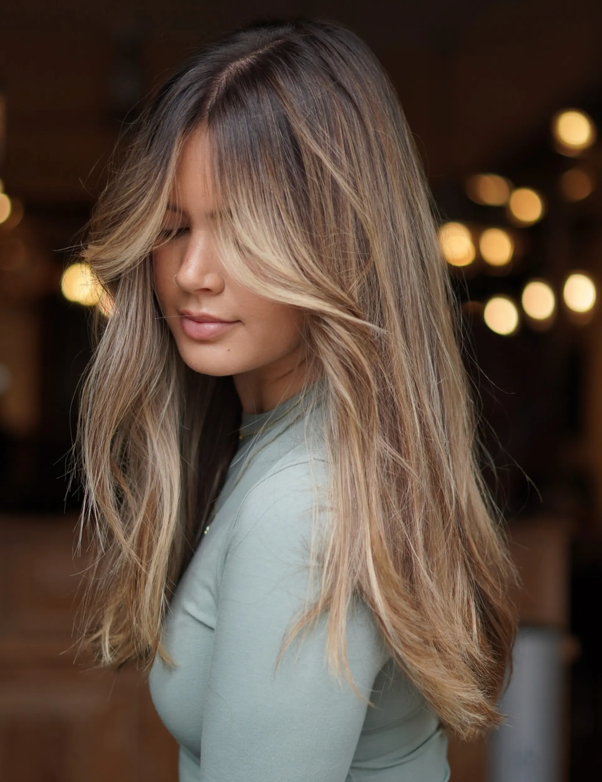 Long layered haircut featuring face-framing curtain bangs and sun-kissed dimensional highlights. 1