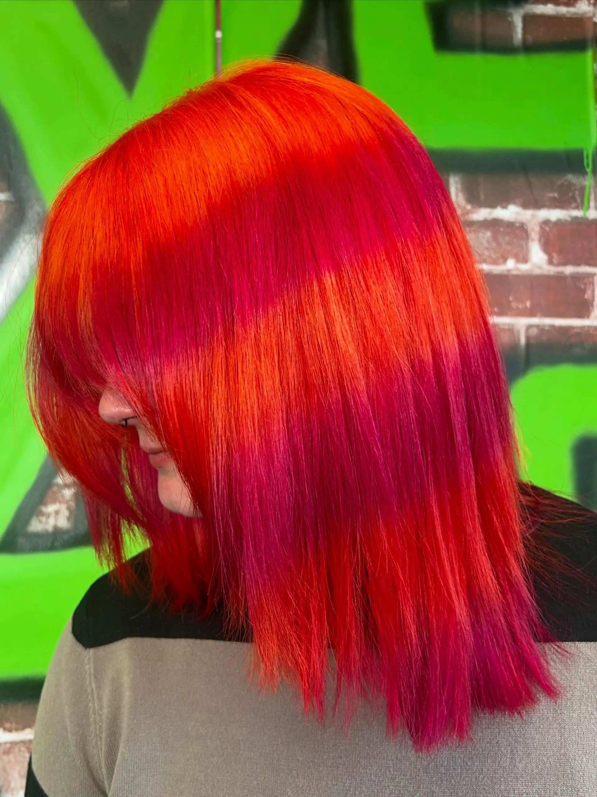 Straight shoulder-length cut with heavy bangs featuring a bold, graphic color block of vivid neon orange and magenta pink. 1