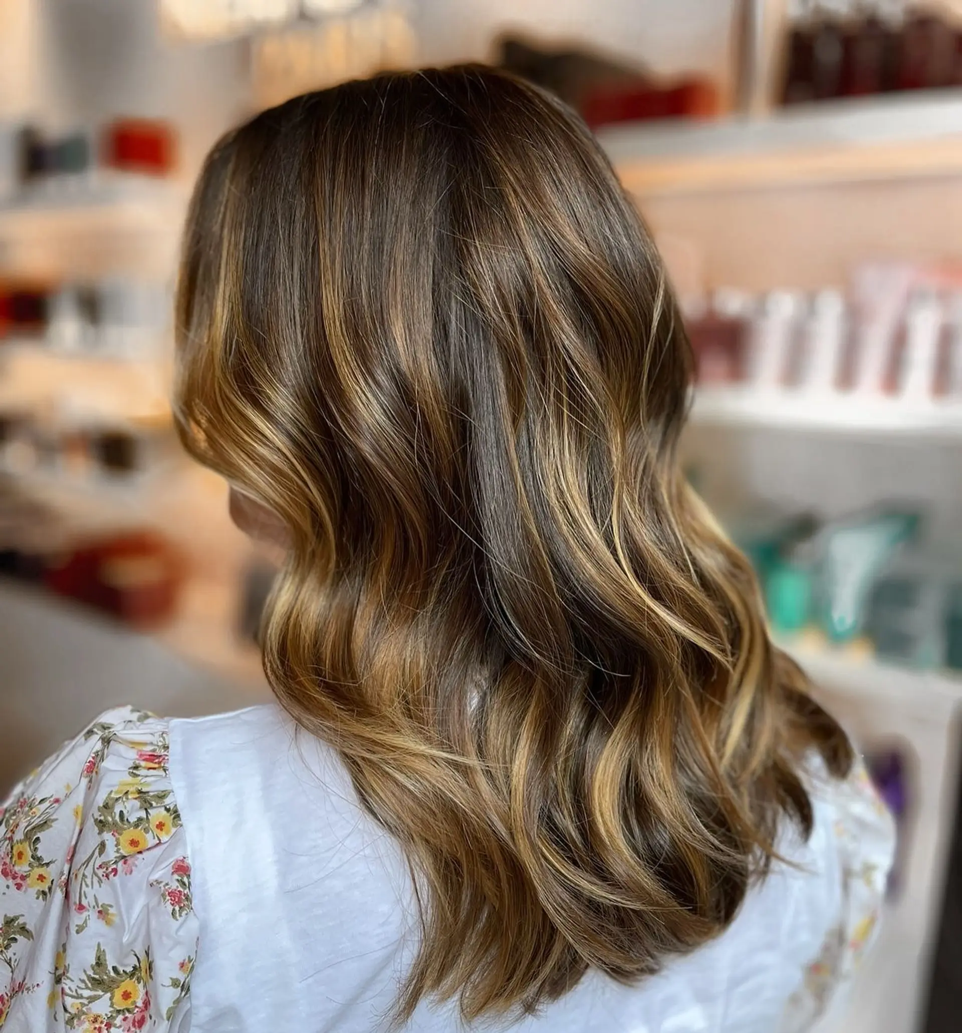 Medium-length brunette hair styled in loose, dimensional waves with hand-painted caramel balayage highlights. 1