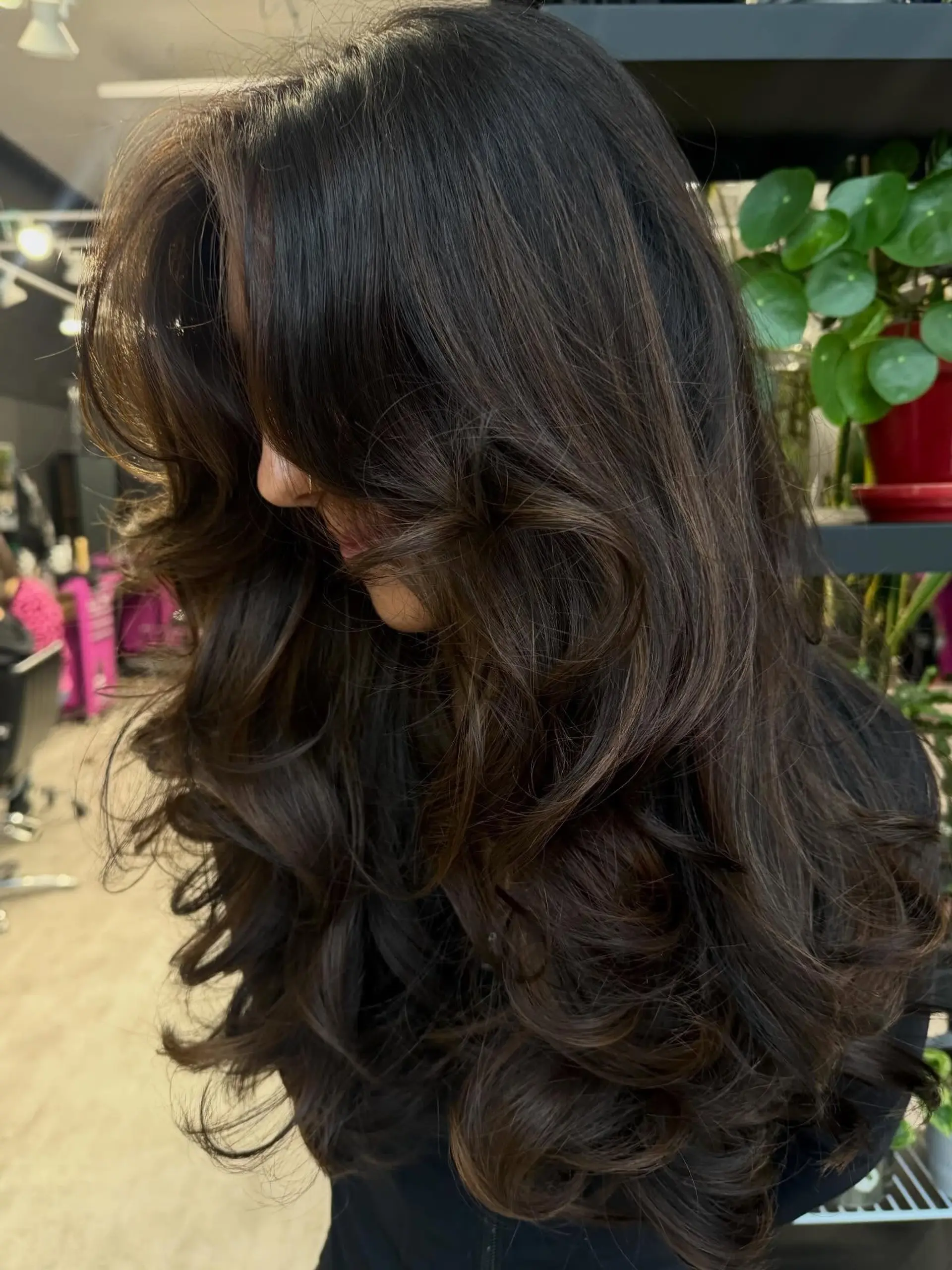 This hairstyle features long, face-framing layers that cascade down, creating significant volume and movement. The ends are styled into soft, bouncy waves, giving the hair a glamorous and full-bodied silhouette. 1