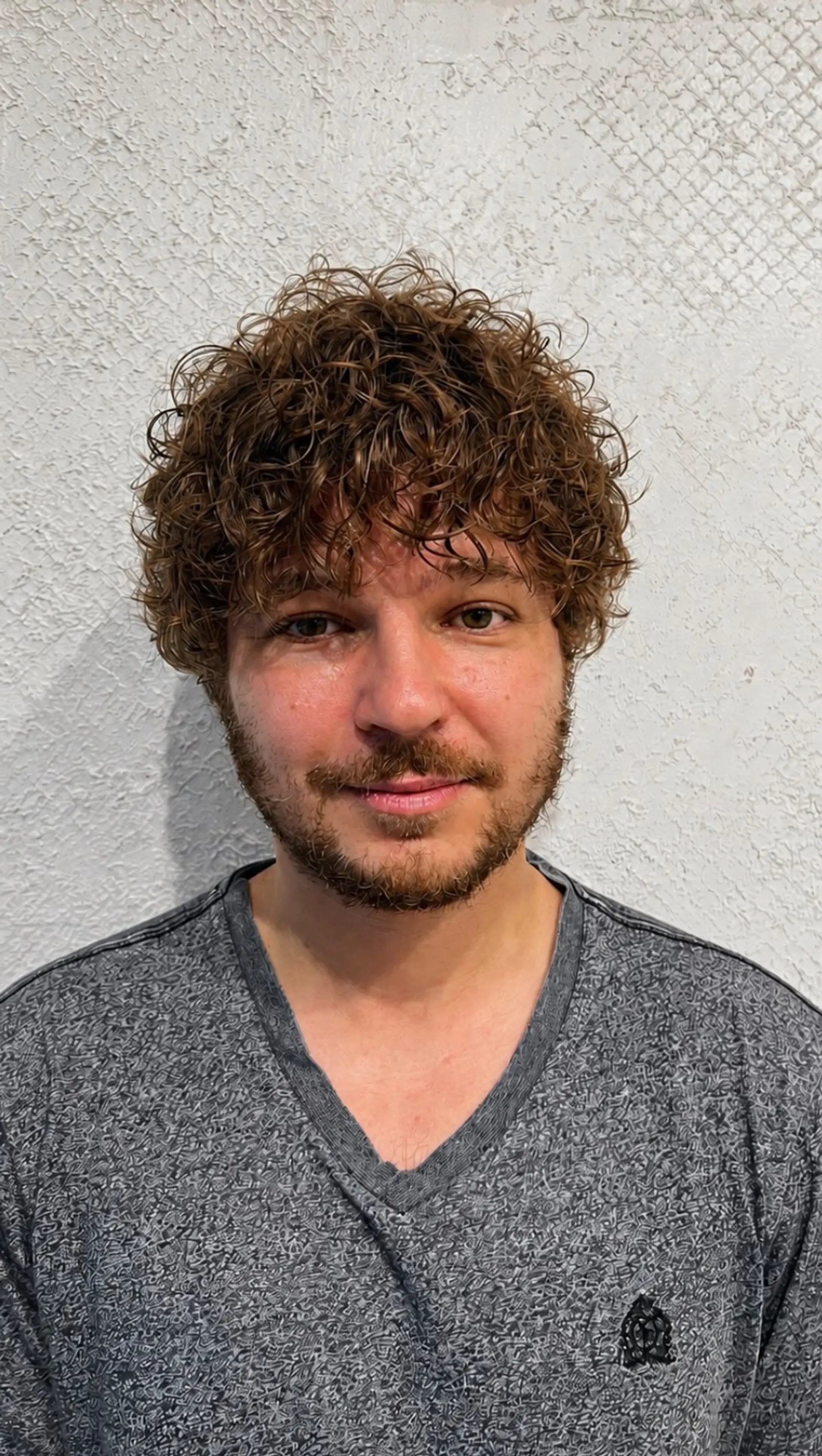 Short layered cut styled with tight, glossy permed curls falling forward into a textured fringe. 1