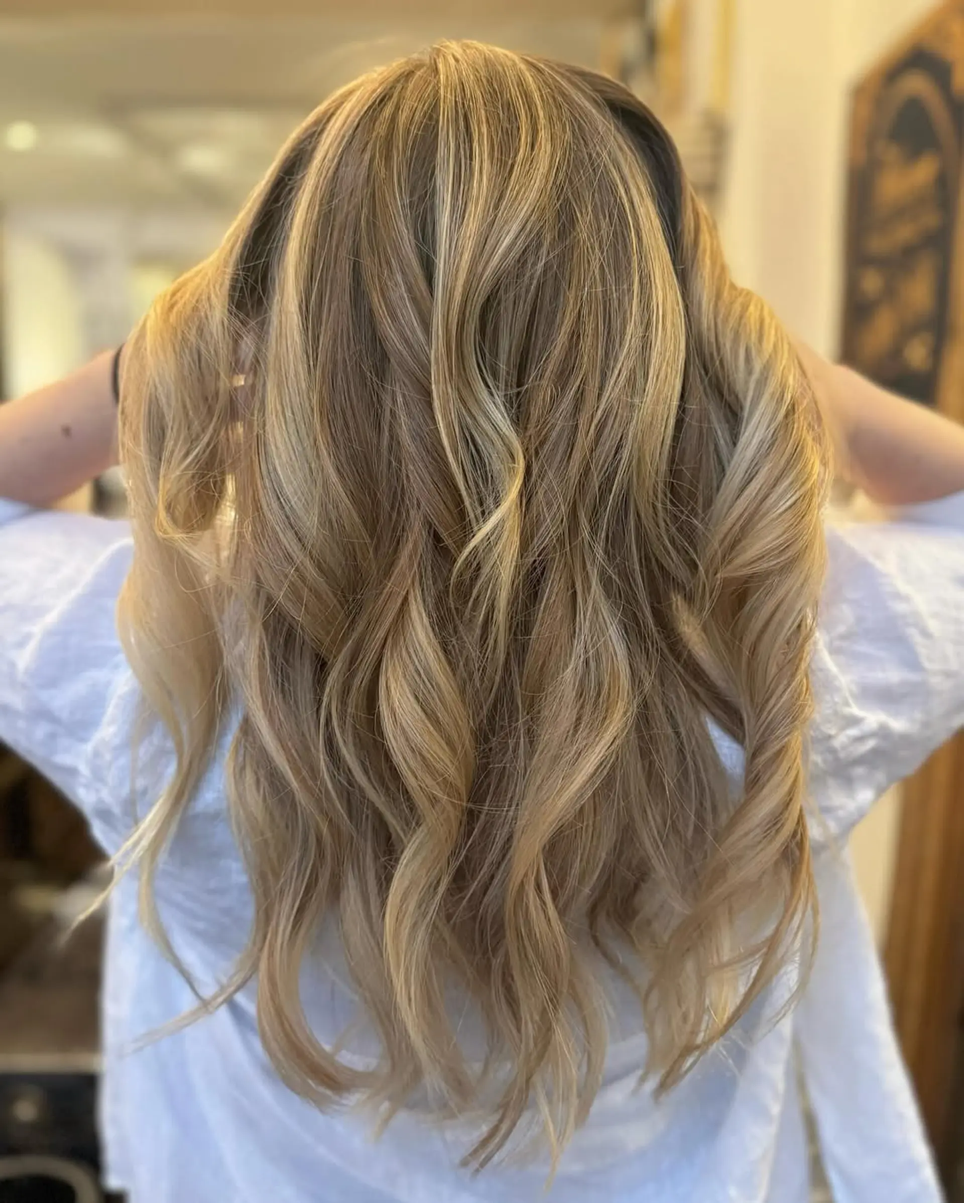 Luxurious long hair with wavy texture, featuring blonde, honey, and caramel shades in a balayage style. The natural highlights and layered ends add softness and movement. 1