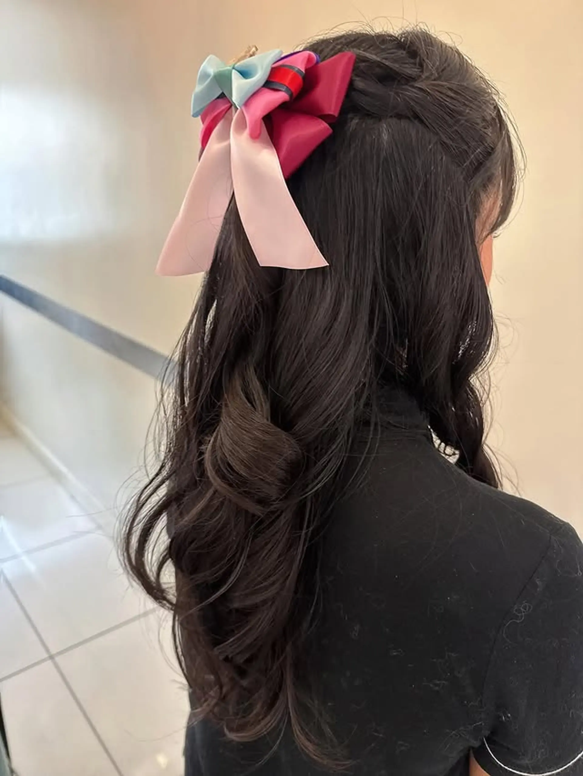 A romantic, twisted half-updo with long wavy hair, accessorized with a colorful bow. 1