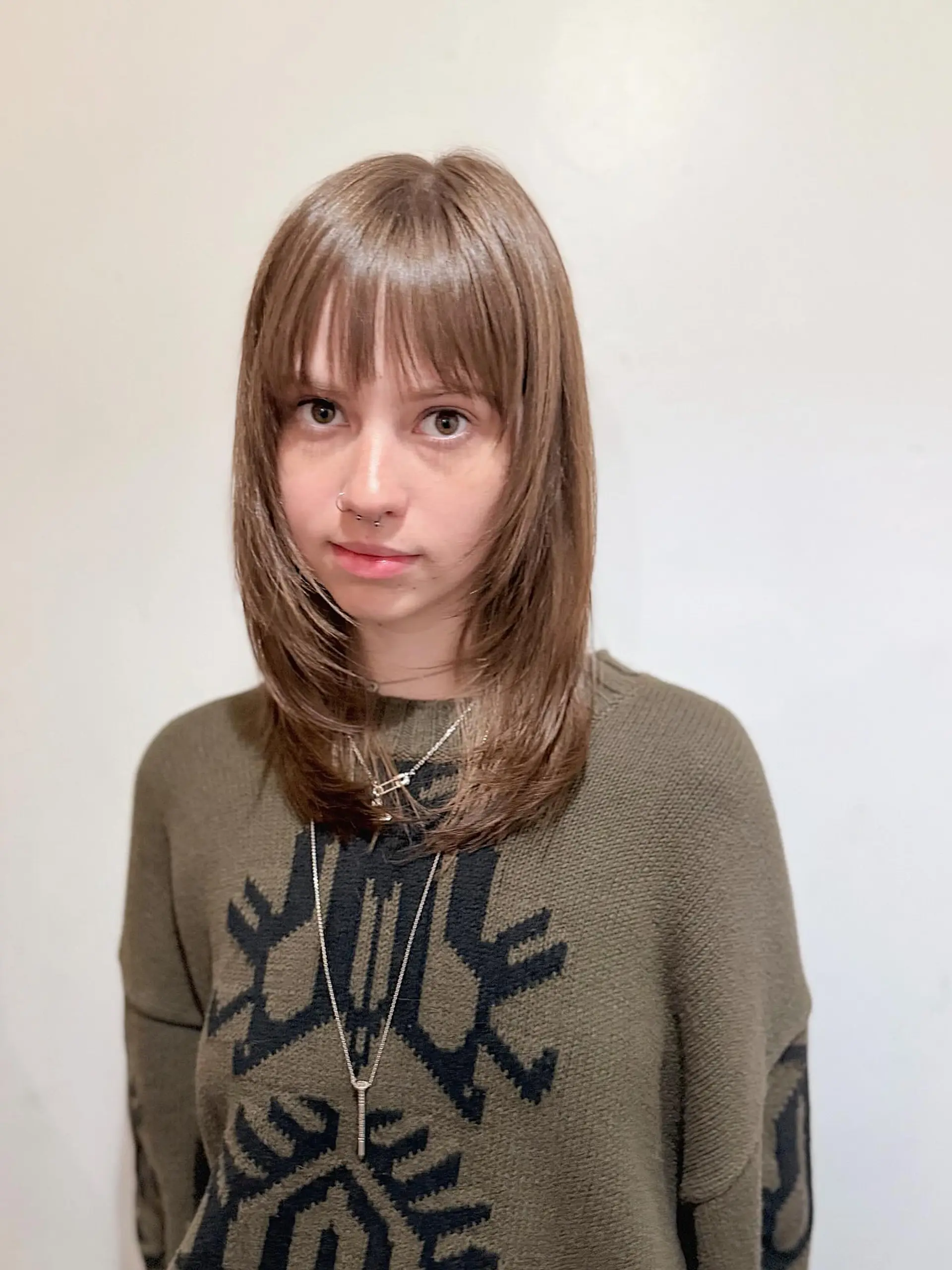 This hairstyle features soft, blended layers that create movement and volume, complemented by a full, straight fringe that frames the face beautifully. The length falls around the collarbone, making it a chic and adaptable cut. 1