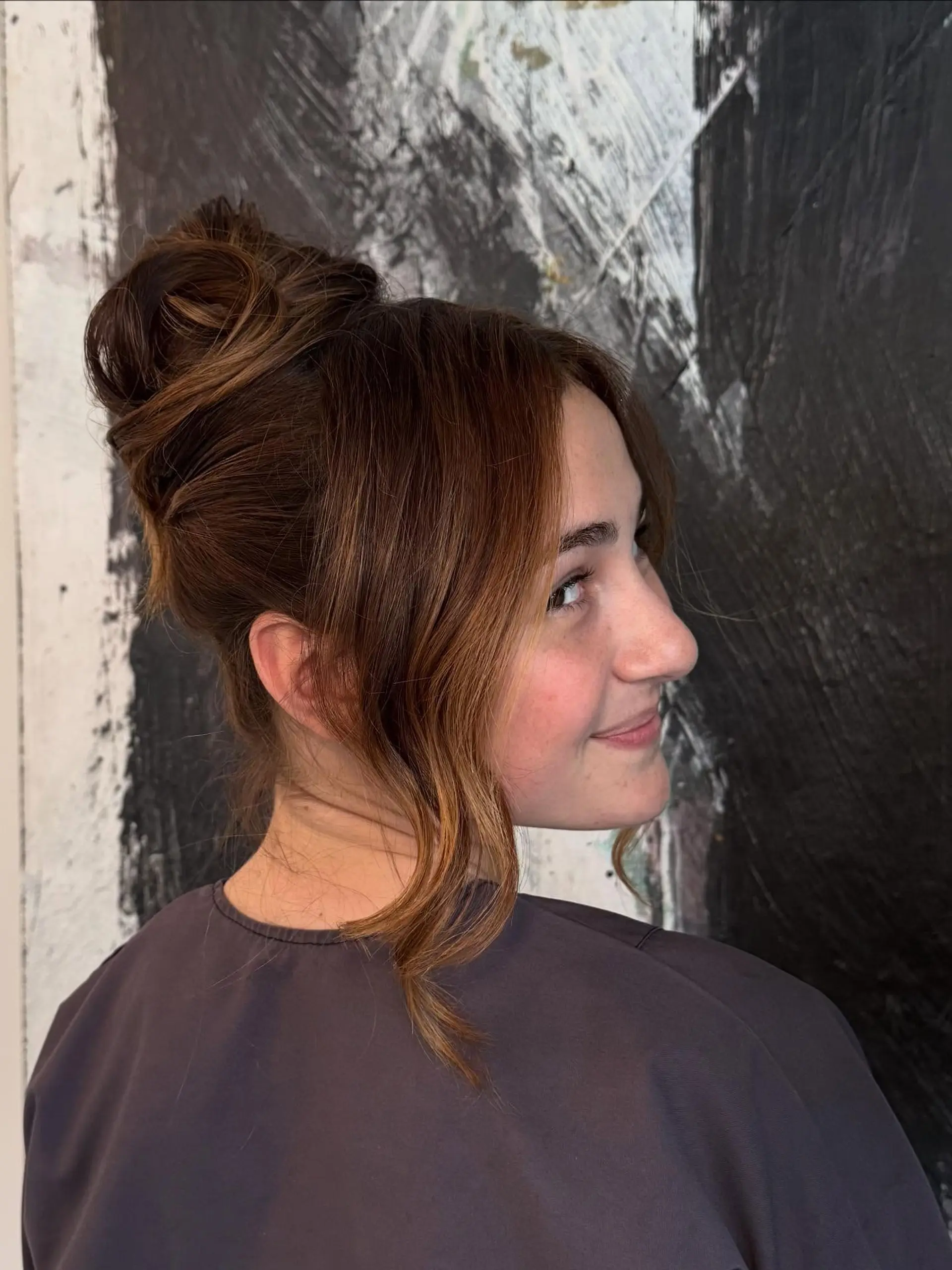 A sophisticated high bun updo sculpted at the crown with soft, wavy face-framing tendrils left loose around the cheeks and neck. 1