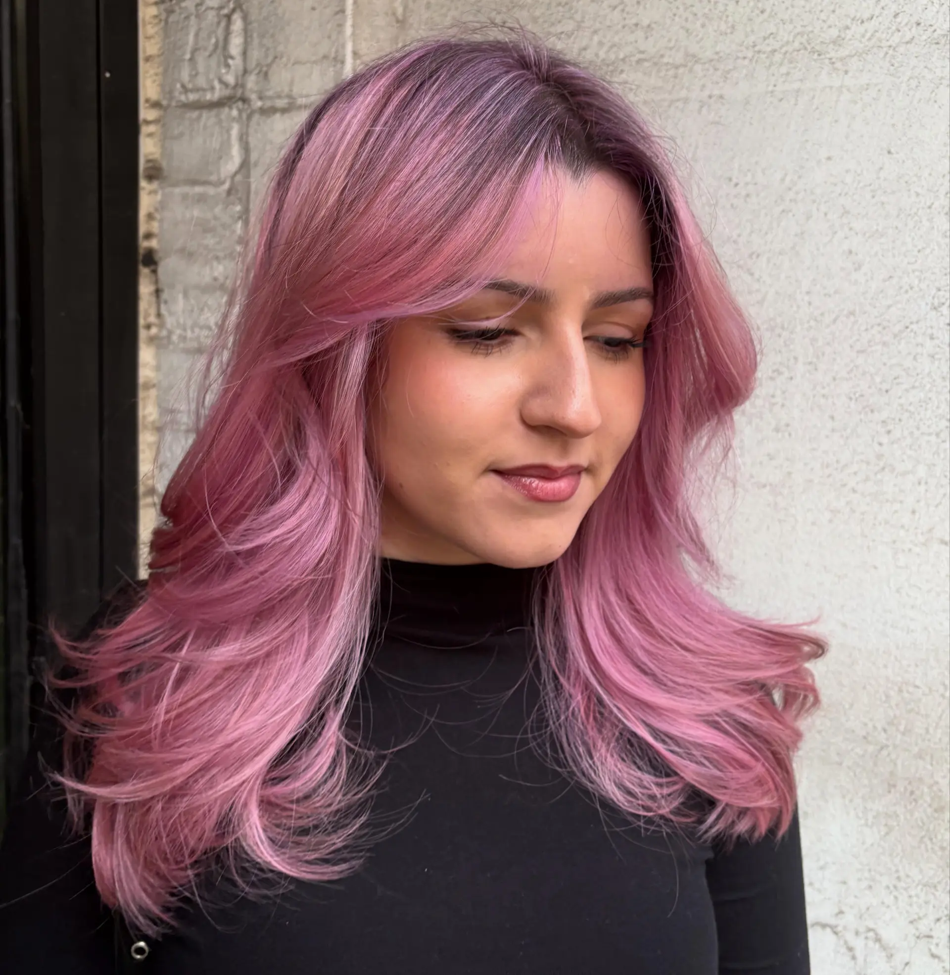 Long pastel pink hair styled into a voluminous blowout with curtain bangs and outward flipped layers. 1