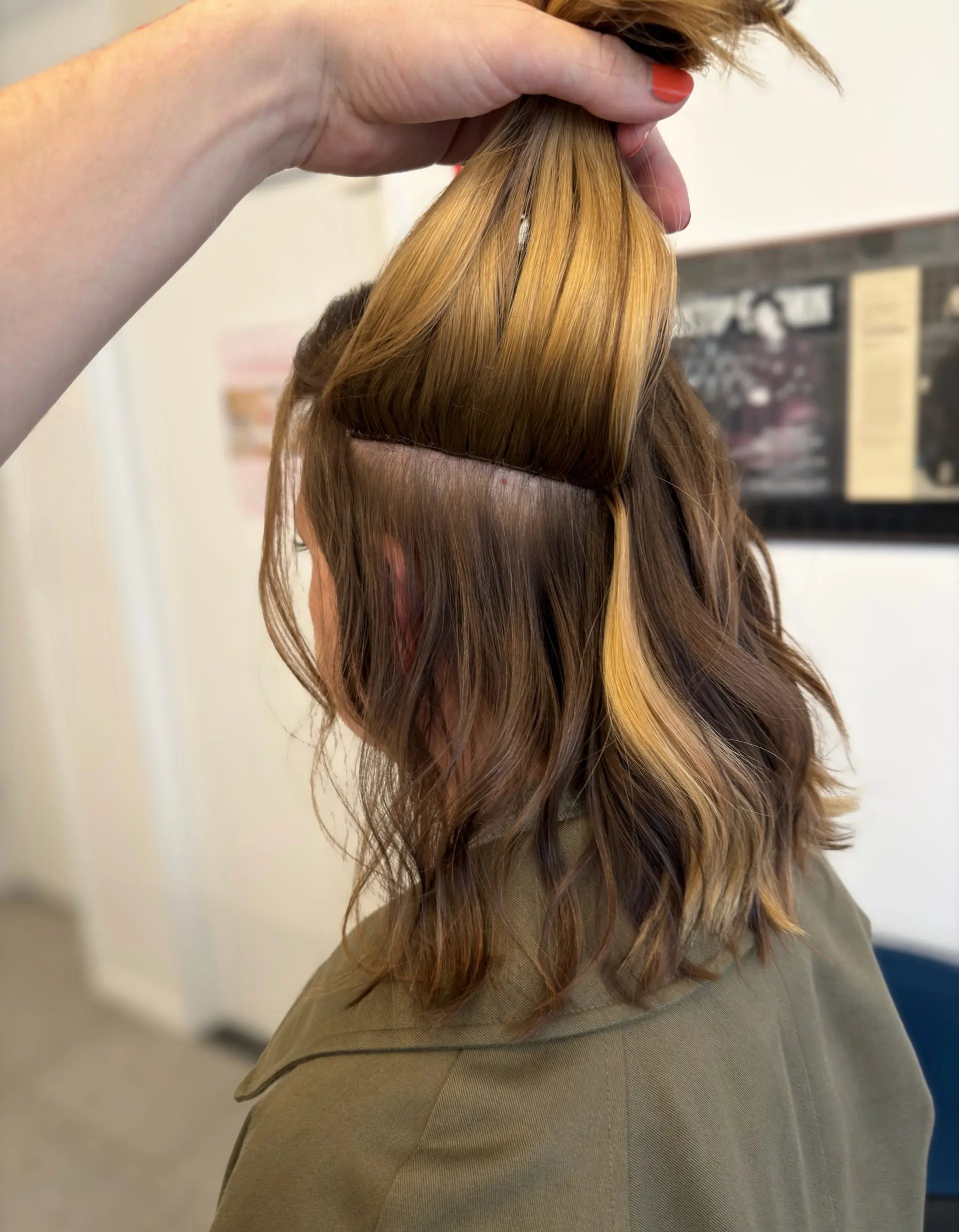 Hand-tied hair extensions demonstrated beneath lifted warm blonde and brown wavy hair. 1
