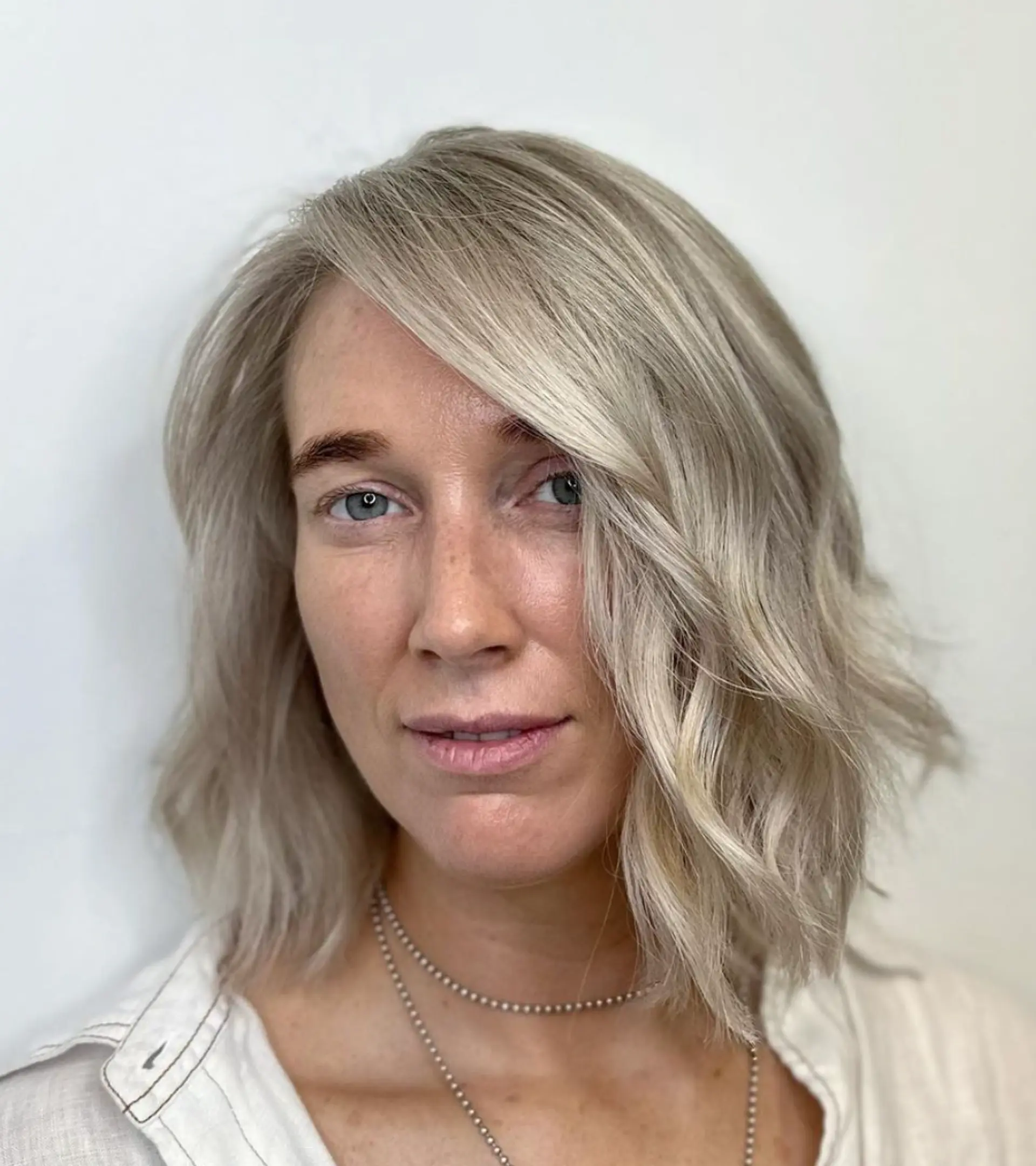 A medium-length, wavy hairstyle with a side part and textured ends, colored in icy silver and platinum shades.

Color by @simabeautynyc
Cut by @juliamannino_hair
 1