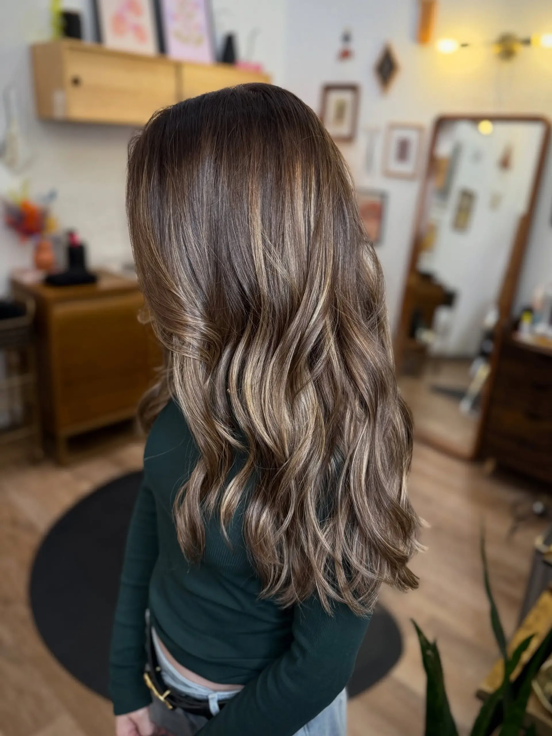 Long dimensional brunette hair styled with soft, cascading waves and seamless golden-caramel balayage highlights throughout. 1