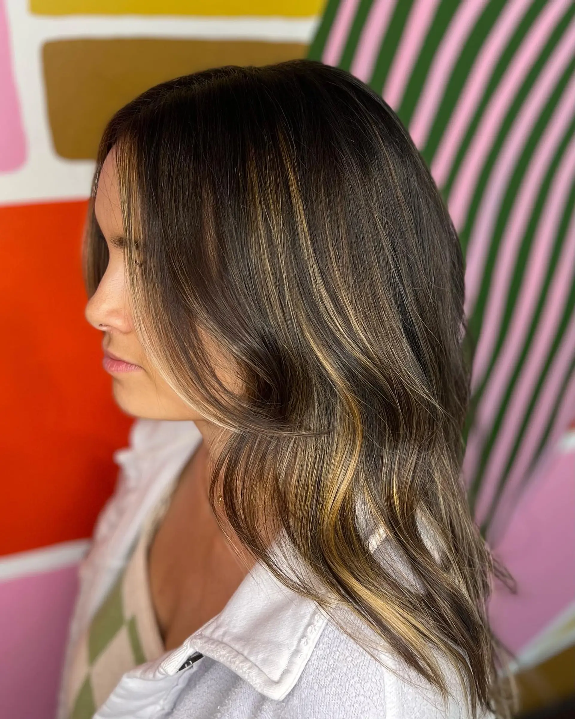 Long dark brunette hair featuring warm caramel balayage highlights and soft waves. 1