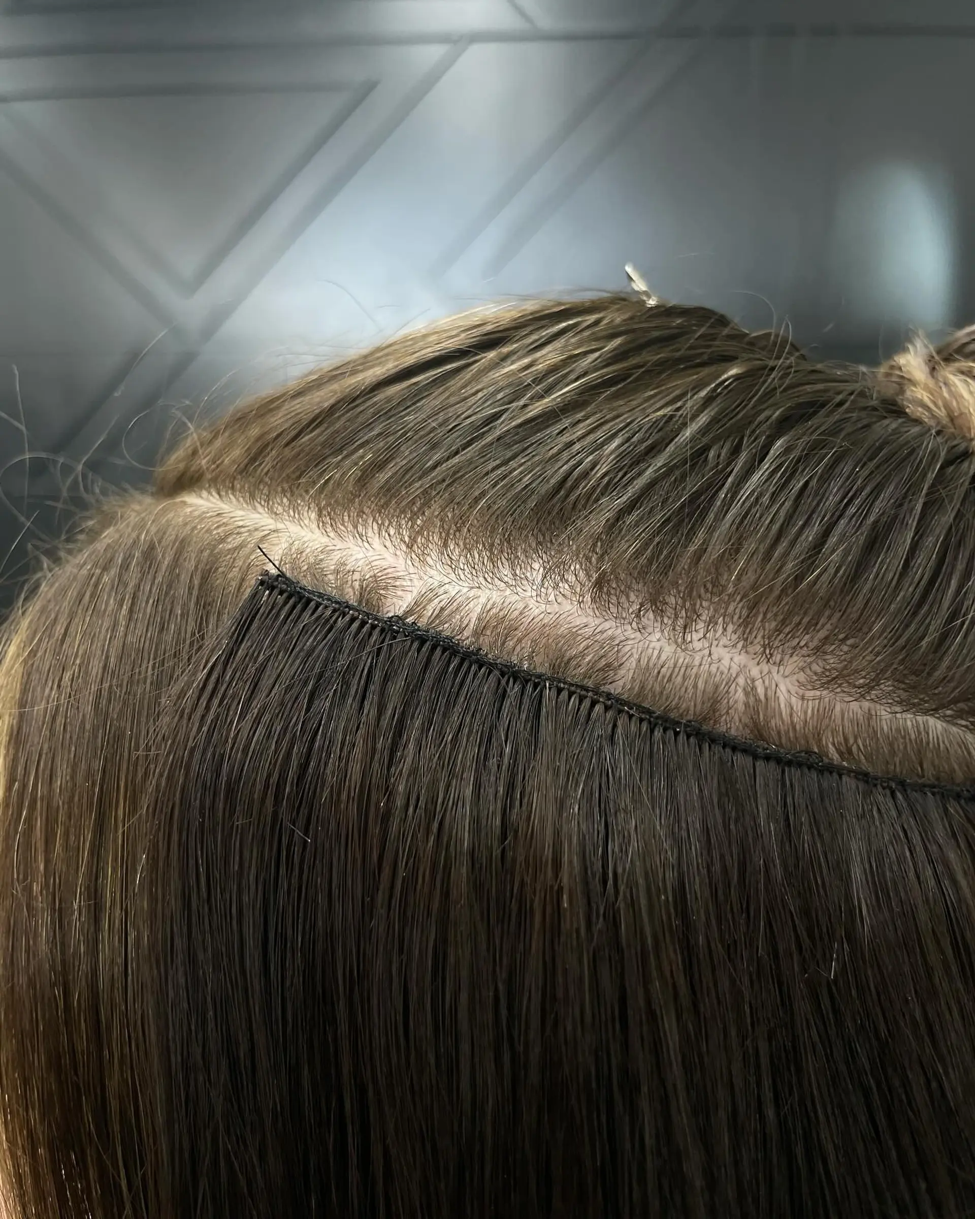Detailed close-up of a seamless hand-tied weft extension installation along a clean horizontal part. 1