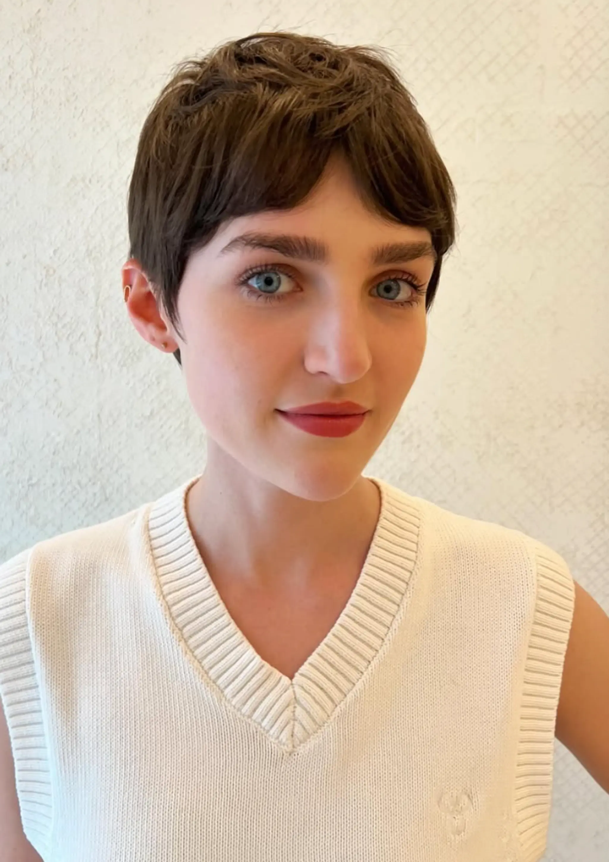 A chic tapered pixie cut with a textured fringe, featuring straight brown hair that is short and neatly styled with a tapered back.