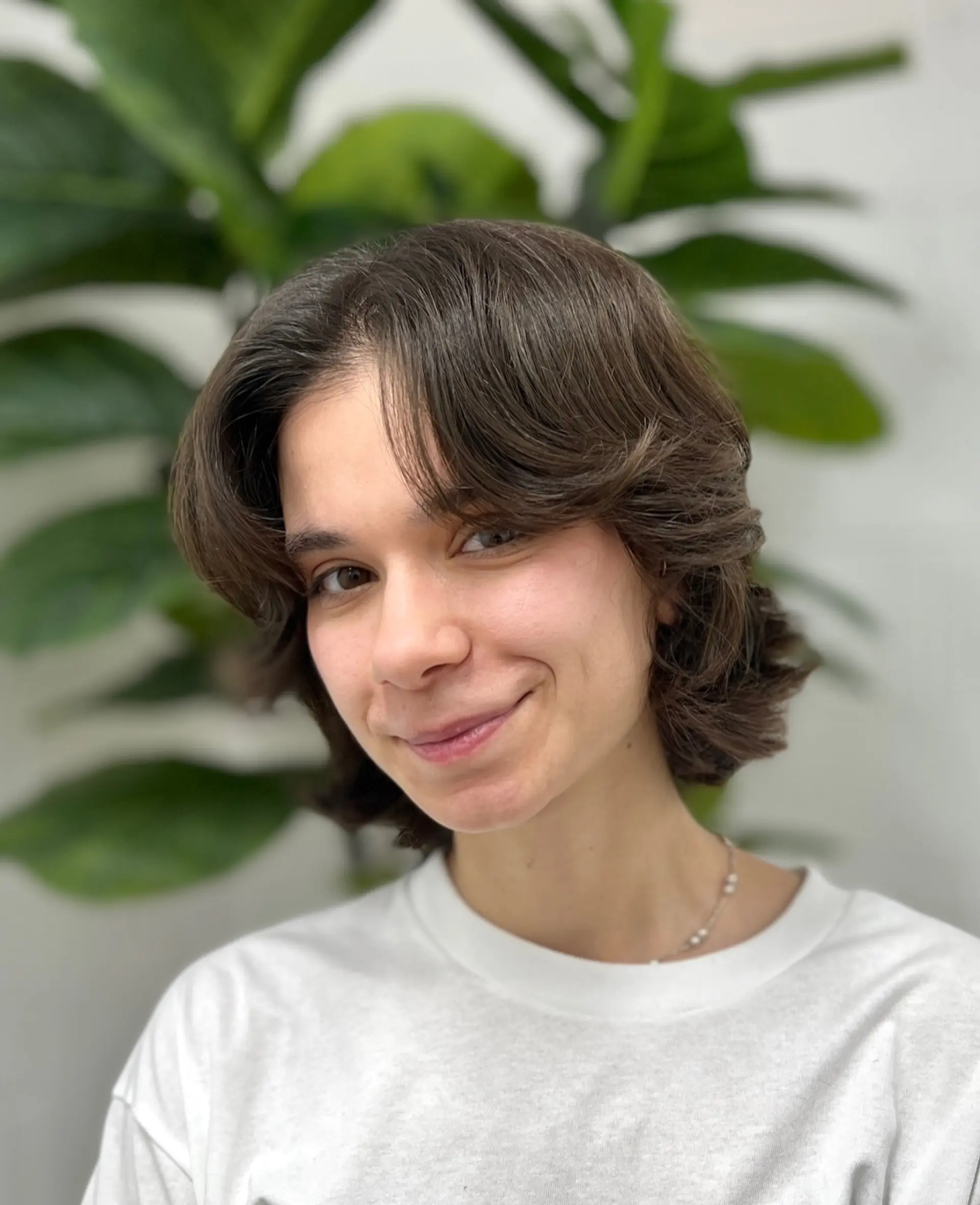 A short brunette layered bob haircut styled with center-parted curtain bangs and textured, flipped-out ends. 1